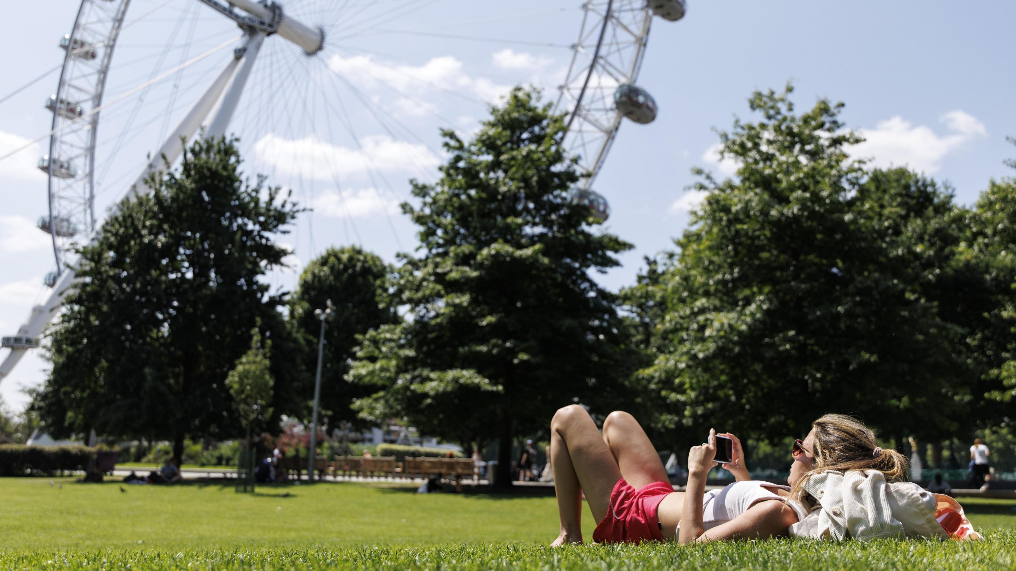 A woman lies in the sun, on the grass, with the London Eye in the background