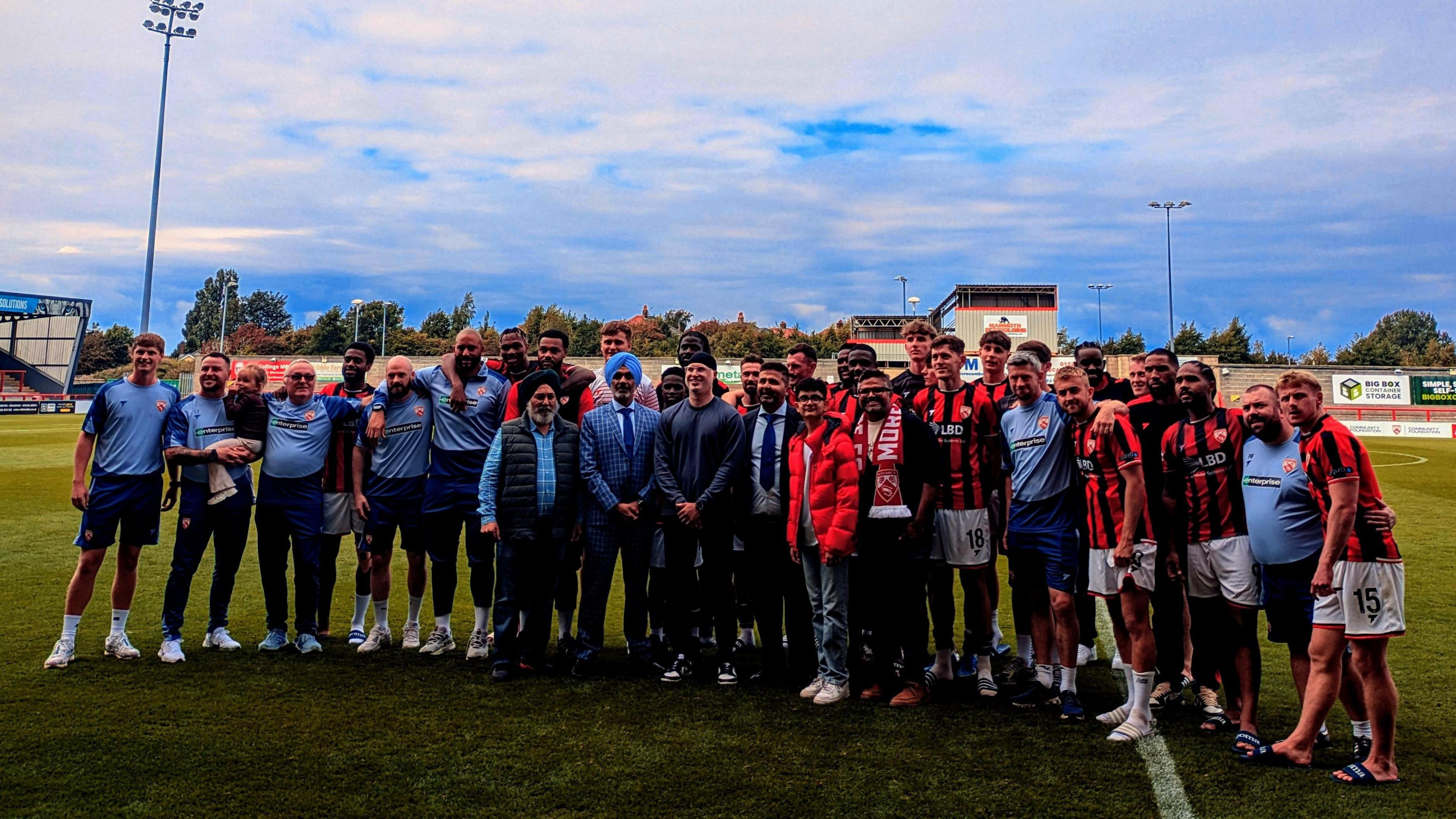 Morecambe players, staff, owners and family members celebrate on the pitch after beating Altrincham 2-1 in the National League