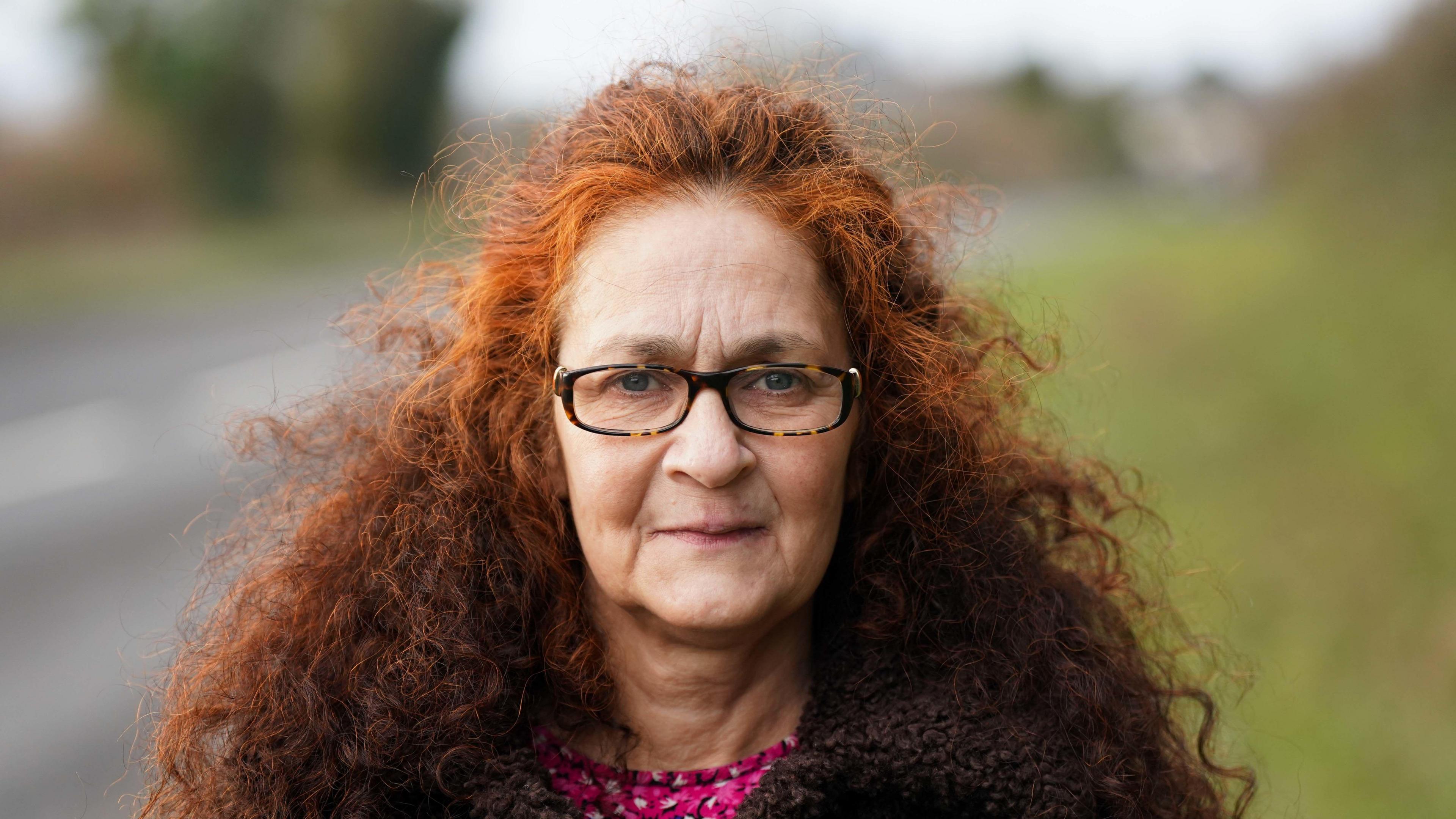 Elizabeth Donowho staring into the camera in a press photo. She has vivid ginger hair and the background is blurred. 