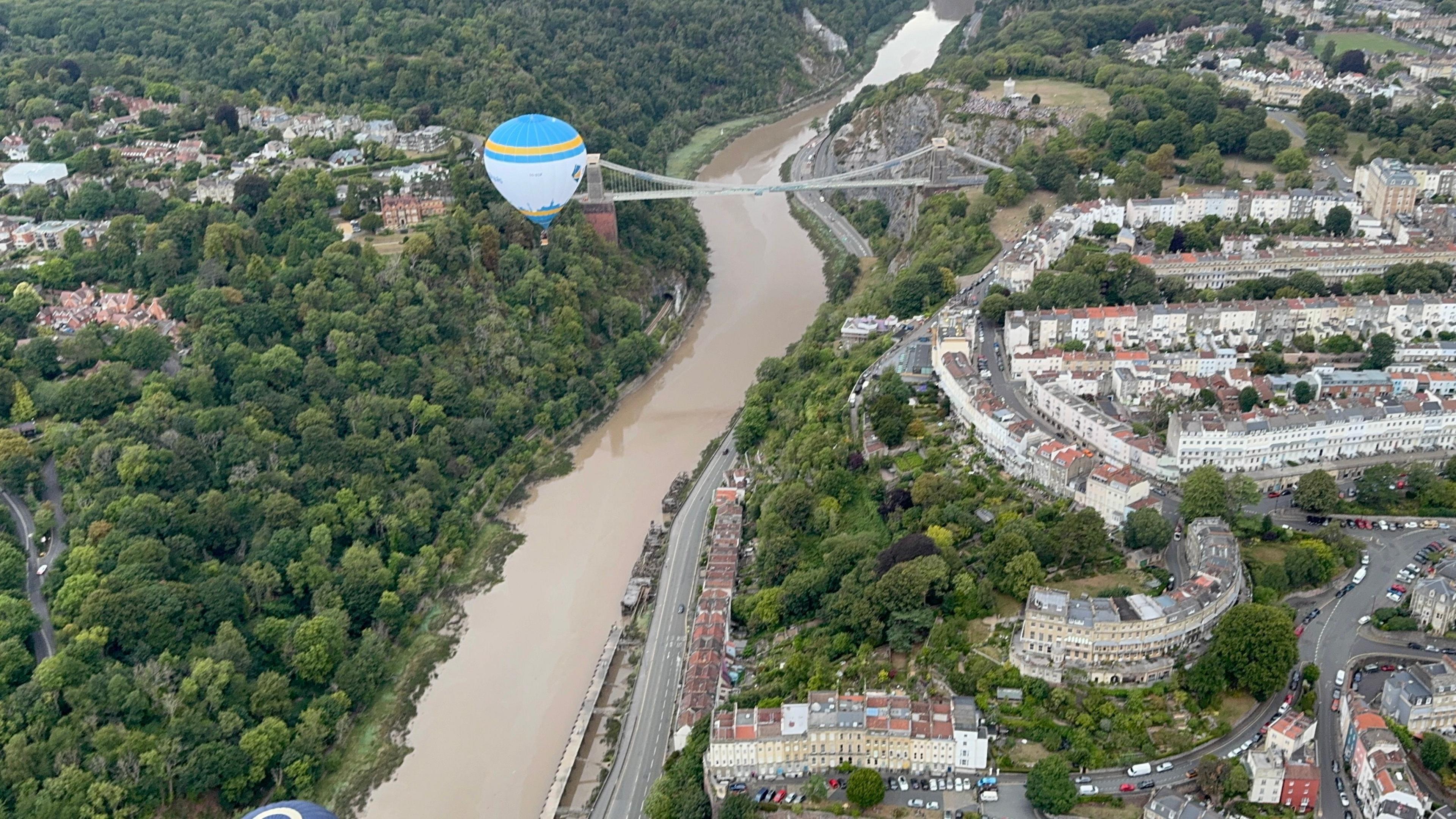 A Bird's Eye view of one blue white and yellow hot air balloon flying past the Clifton Suspension Bridge.