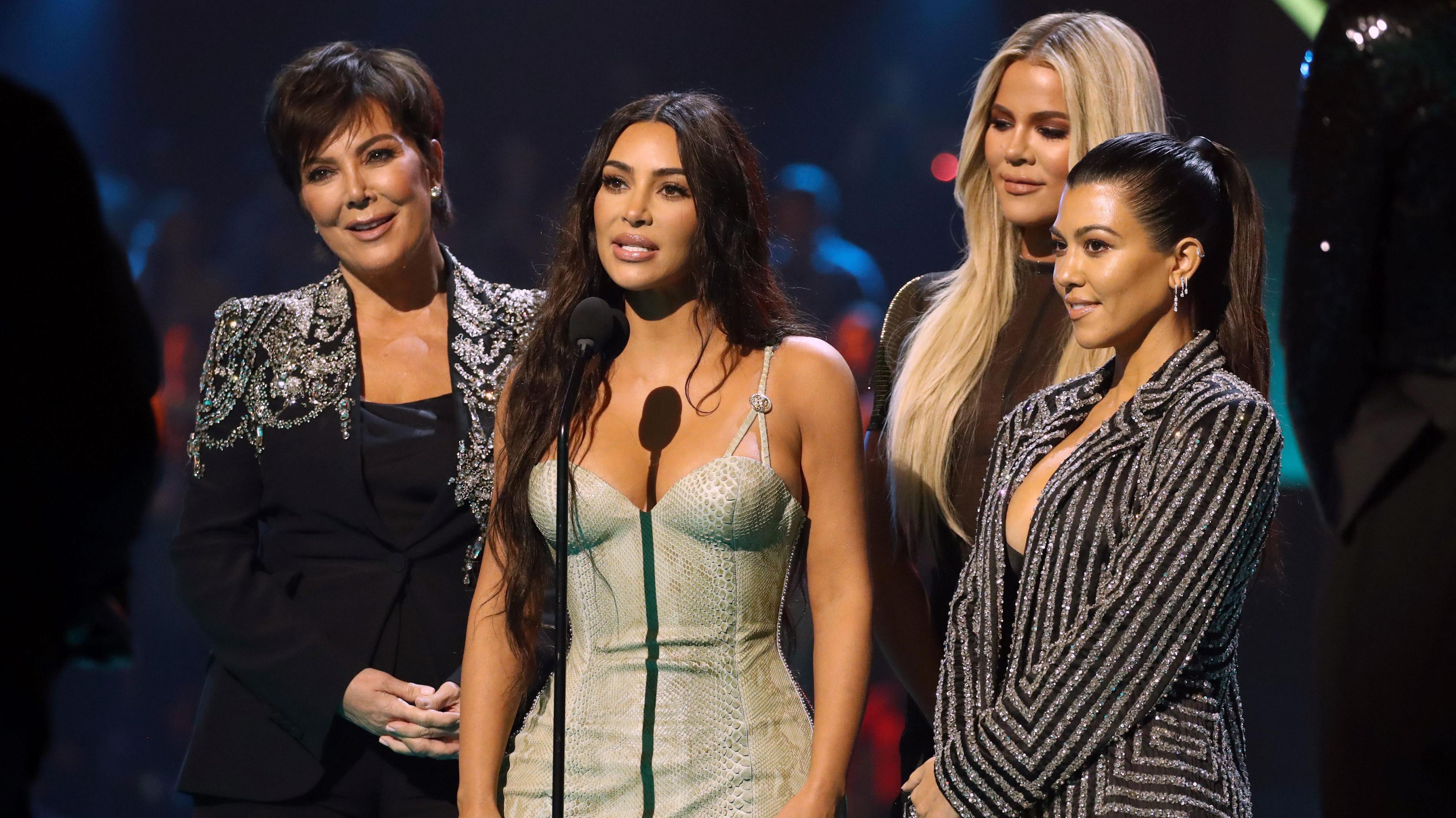 Kris Jenner, Kim Kardashian, Khloé Kardashian, and Kourtney Kardashian onstage at an awards ceremony, dressed in glamourous outfits.