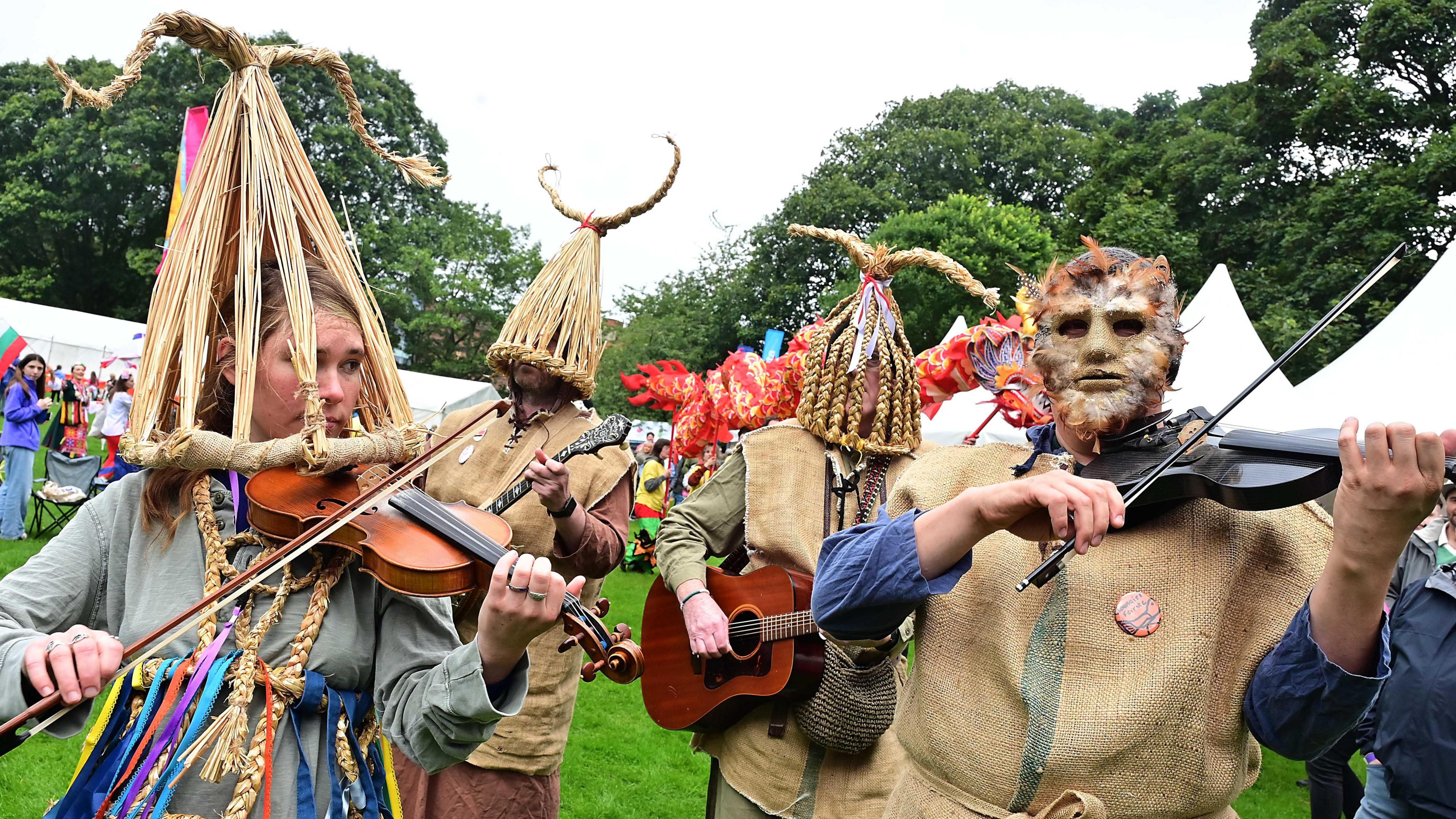 People at festival ground with violins and decorated masks on their heads. 