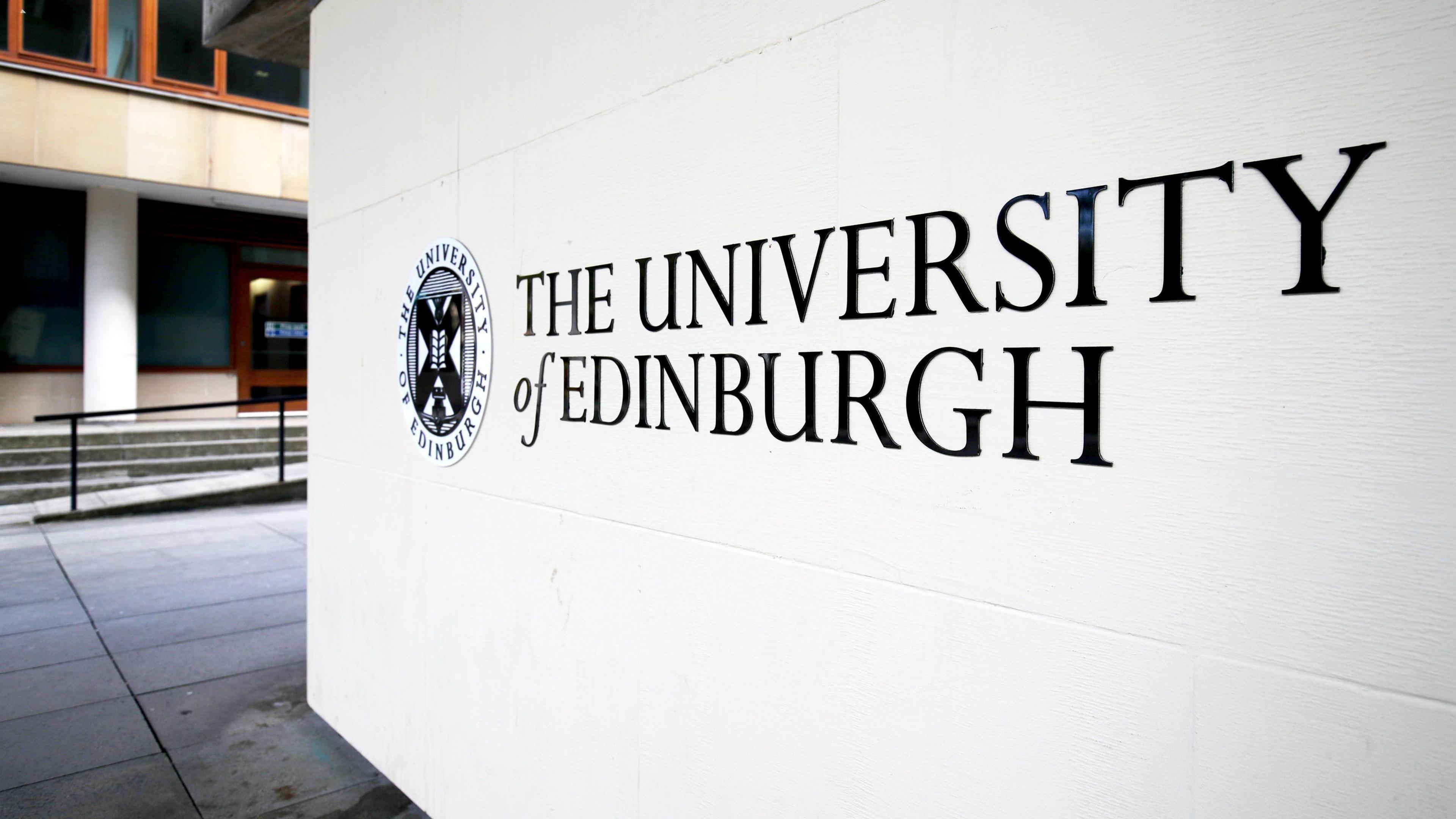 Close up of a white and black University of Edinburgh sign with a building partially visible in the background