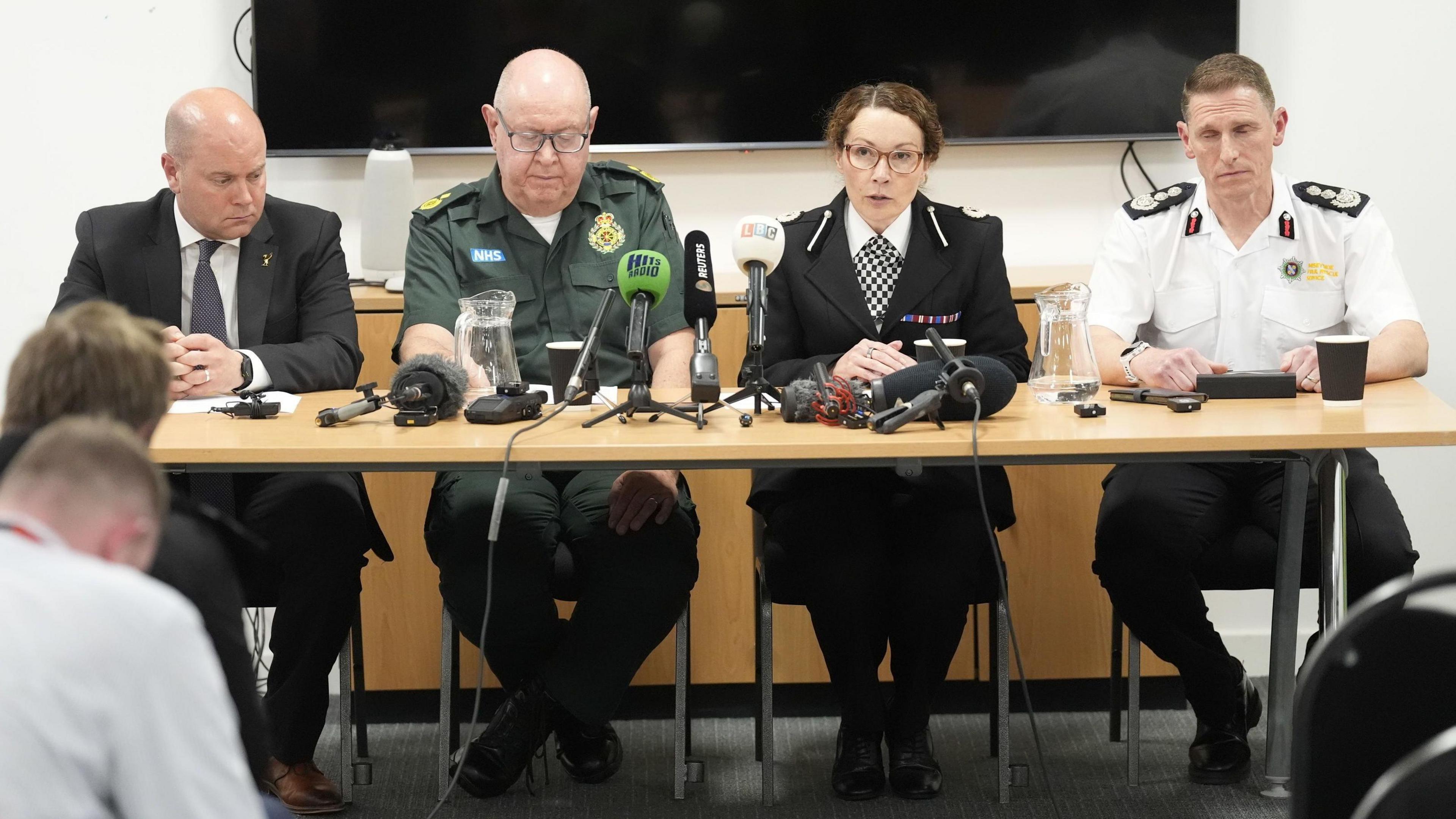 Liam Robinson of Liverpool Council, David Kitchin of NWAS, Ass Ch Con Jenny Sims of Merseyside Police and Nick Searle of Merseyside Fire and Rescue Service sit behind a wooden table lined with microphones and speak to the media.