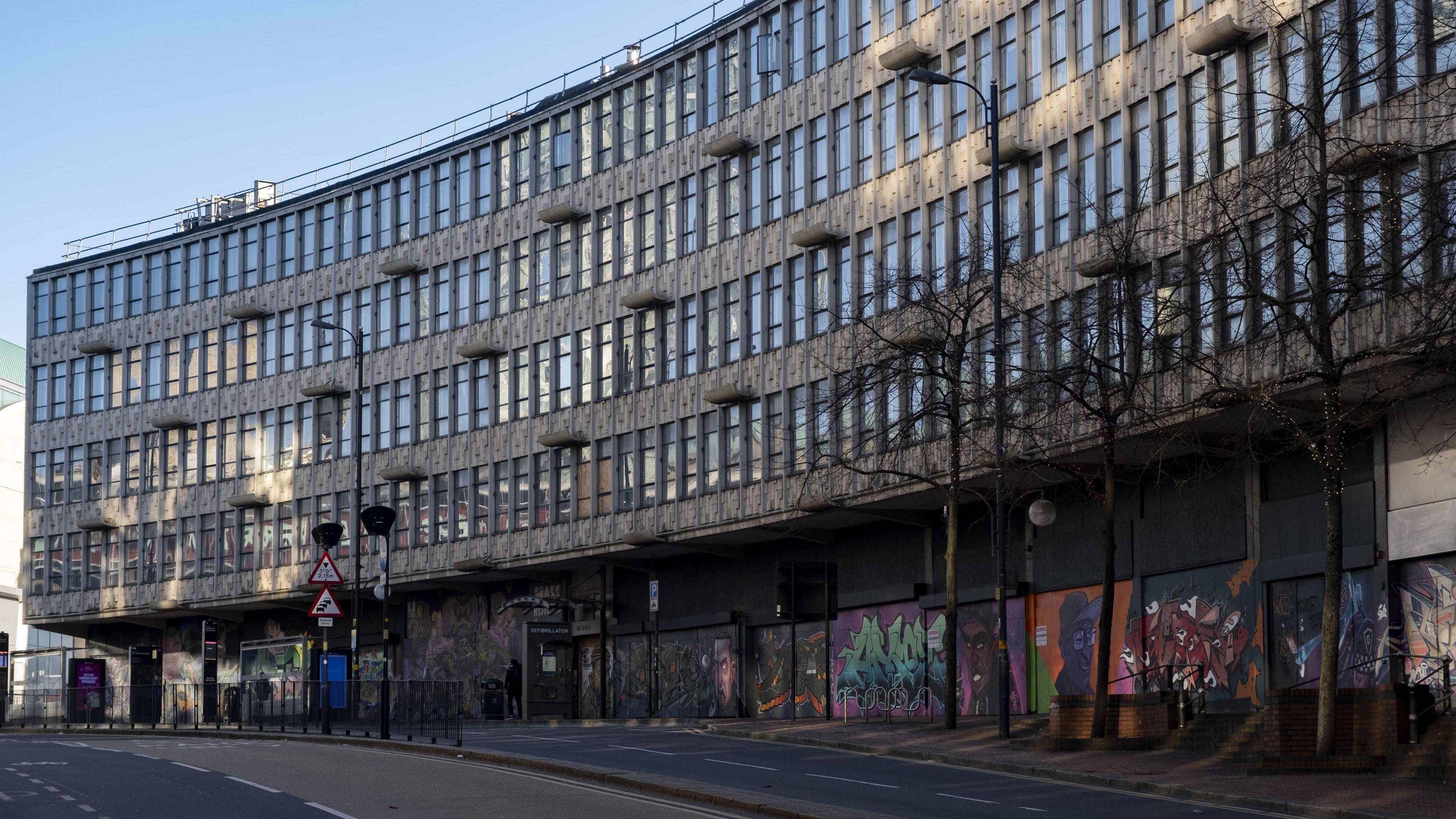 A curved building with grey walls and rectangular windows. There is graffiti on the ground floor.