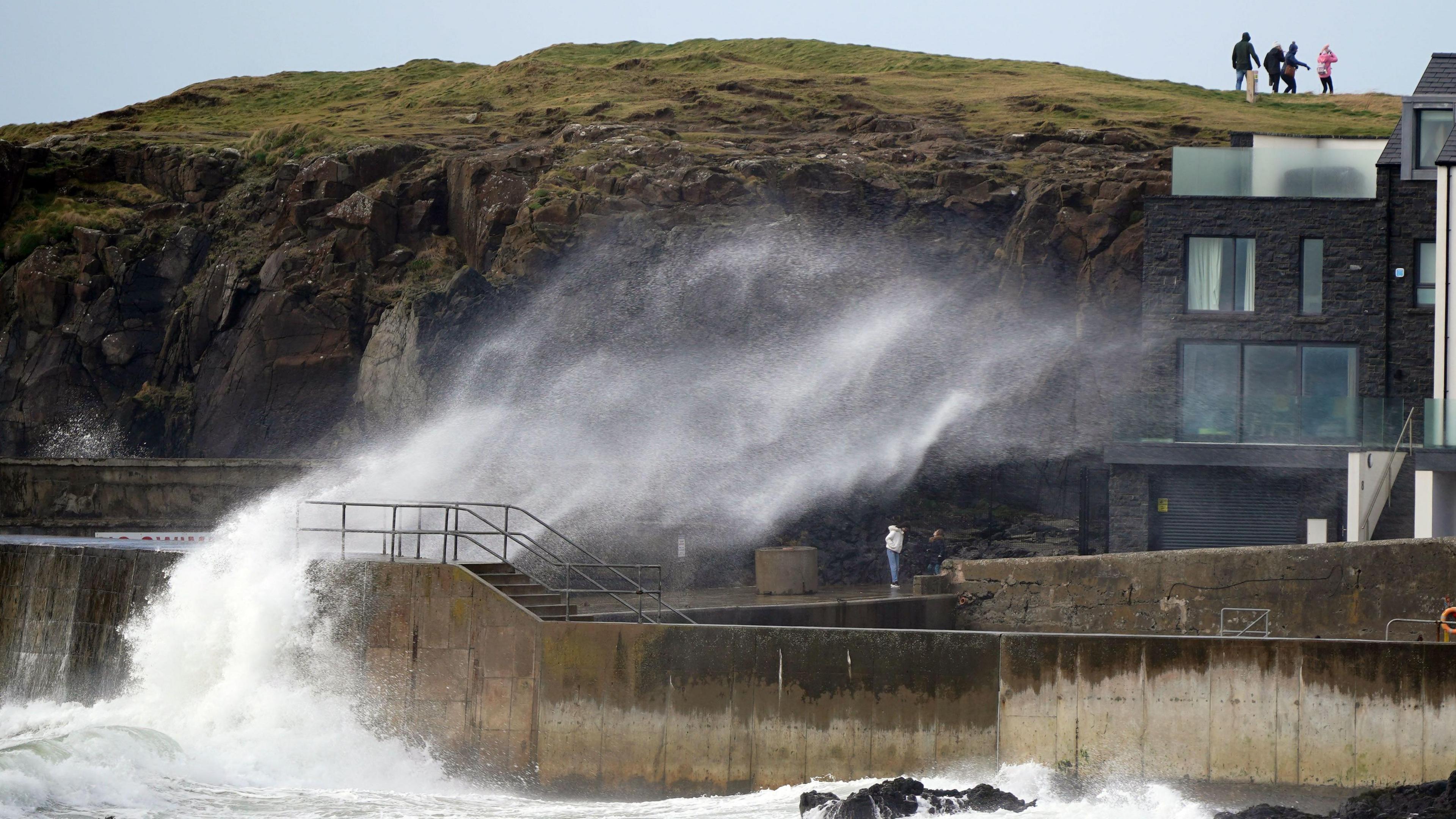 Big waves hit against the sea wall at Portstewart in County Londonderry, Northern Ireland. People can be seen walking on top of the cliff.