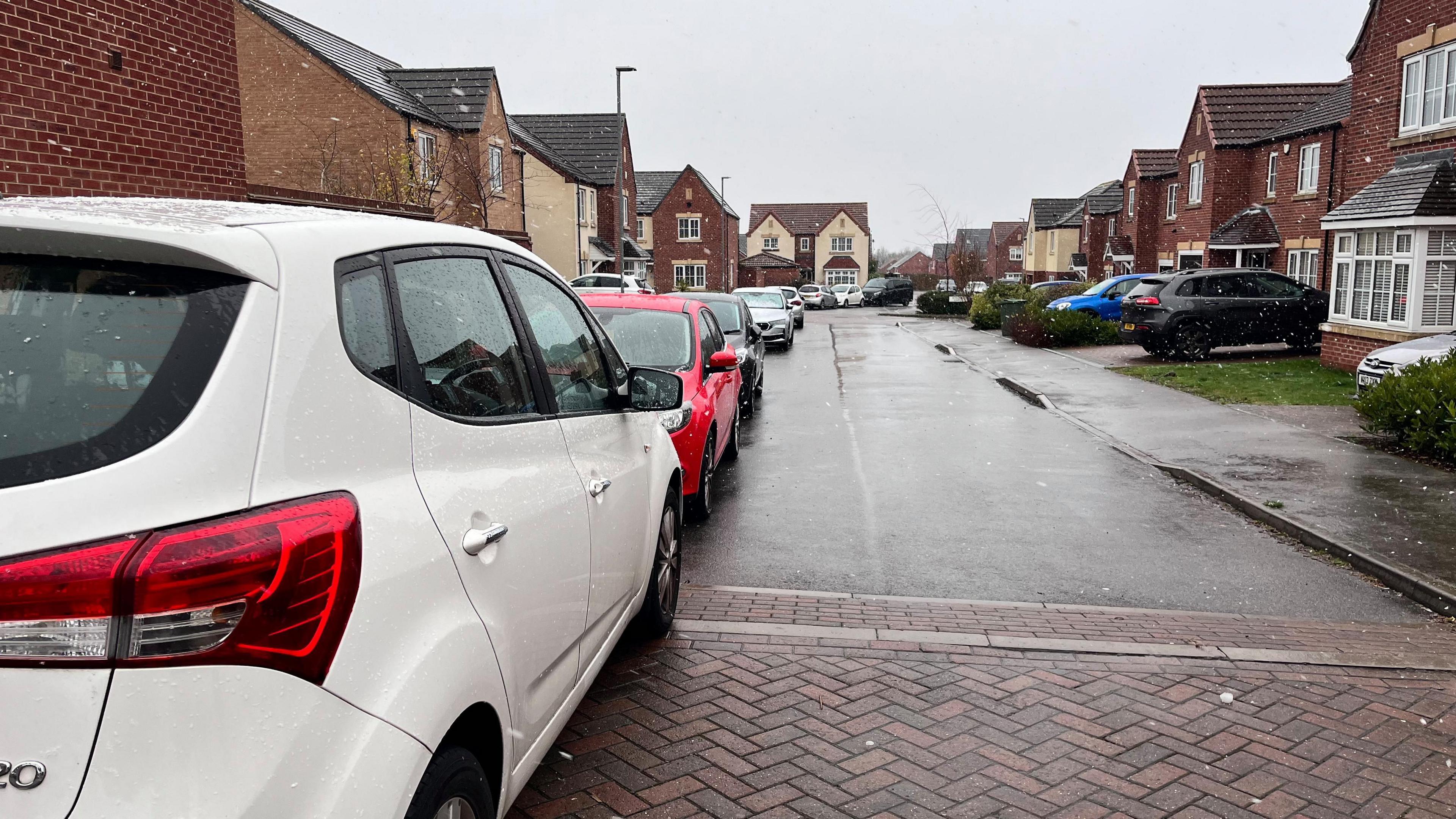A row of cars can be seen parked all the way down a residential street close to Castle Hill Hospital. There are houses and gardens on either side.