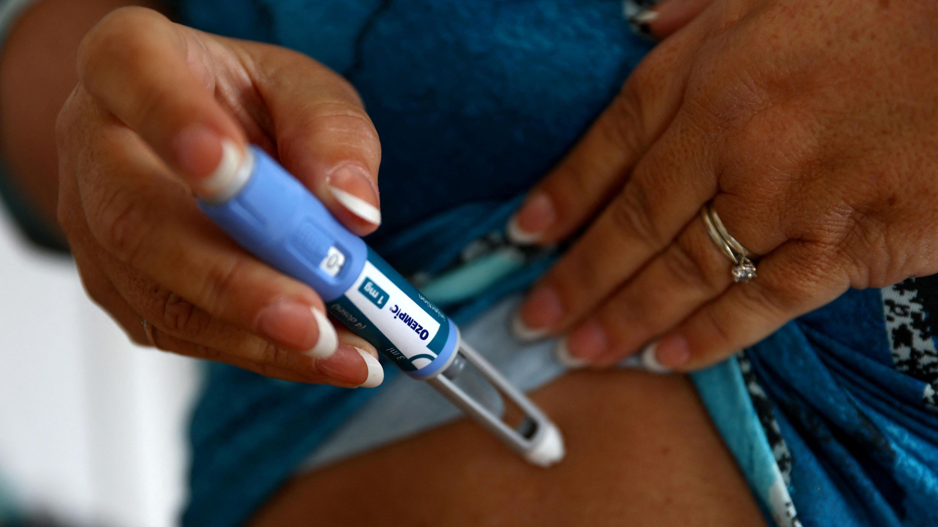 A close up of a woman's hands - she is holding an injection pen and is about to inject a weight  loss drug into her abdomen. 