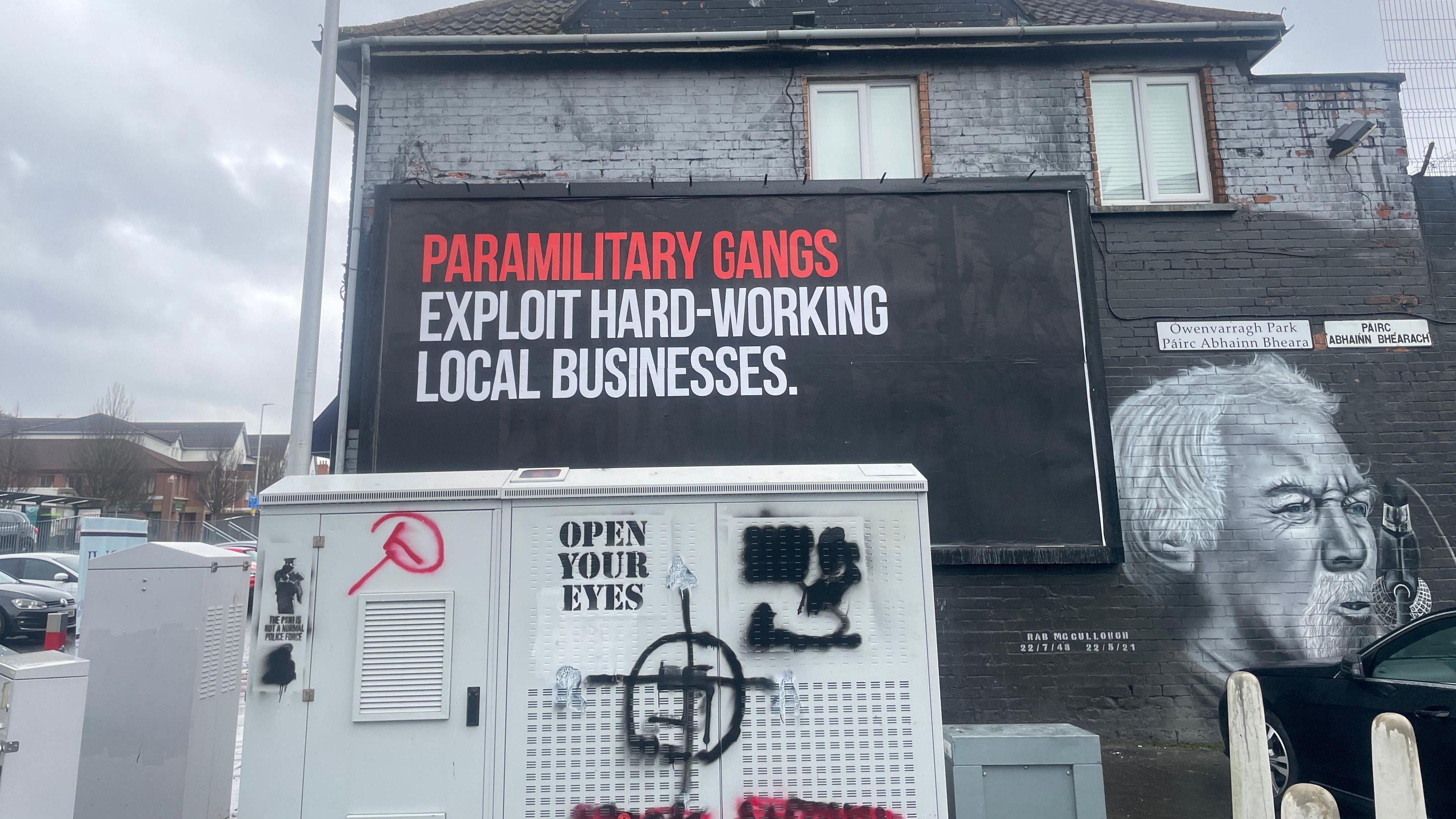 A sign on the side of a building saying: "Paramilitary gangs exploit hard-working local businesses." 