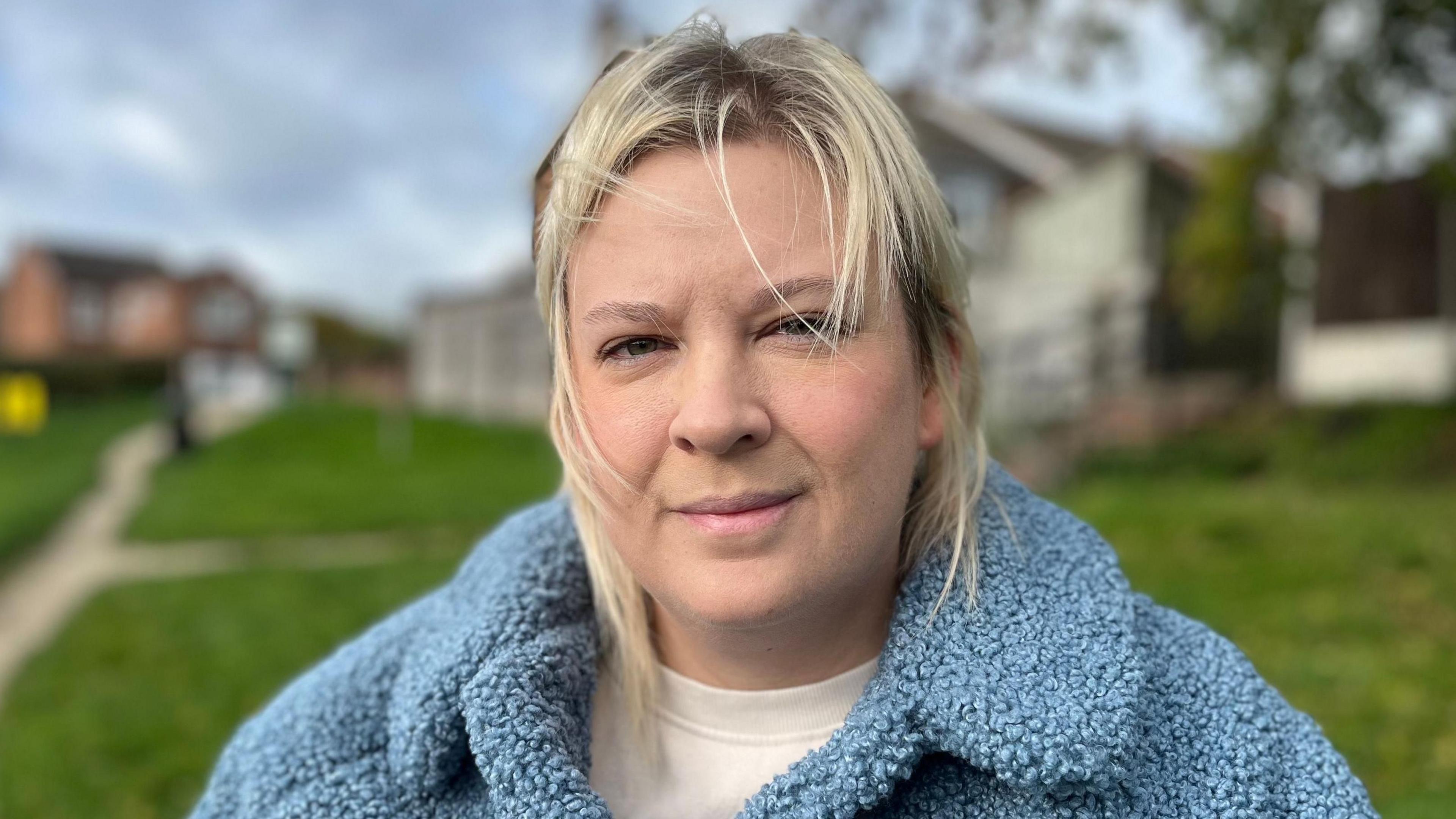 Natalie Elliott with shoulder length blonde hair looking at the camera. She is wearing a light blue woolly jacket.
