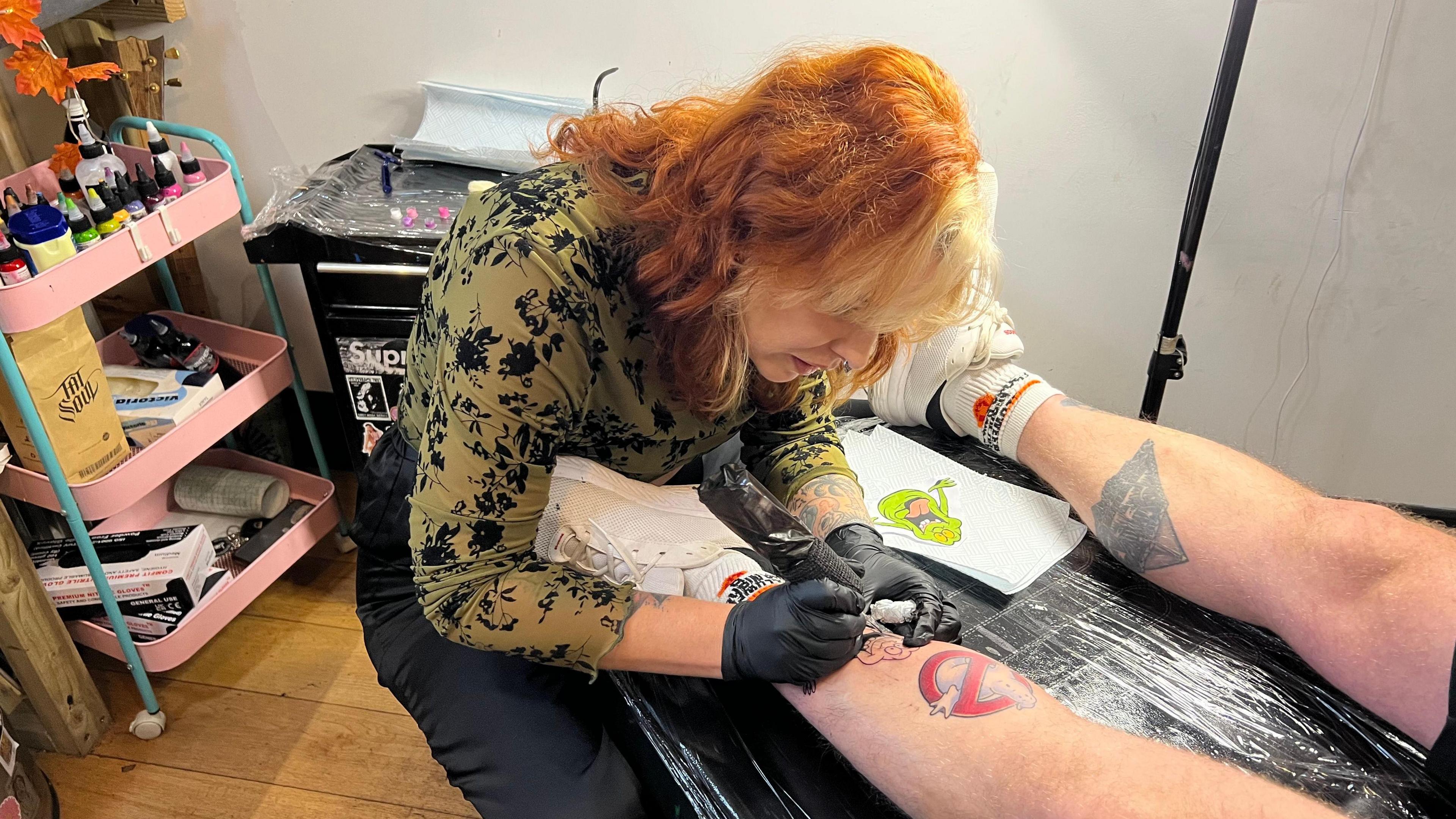 Tattoo artist Holly Dosdale at work. She is working on a tattoo on a man's leg.