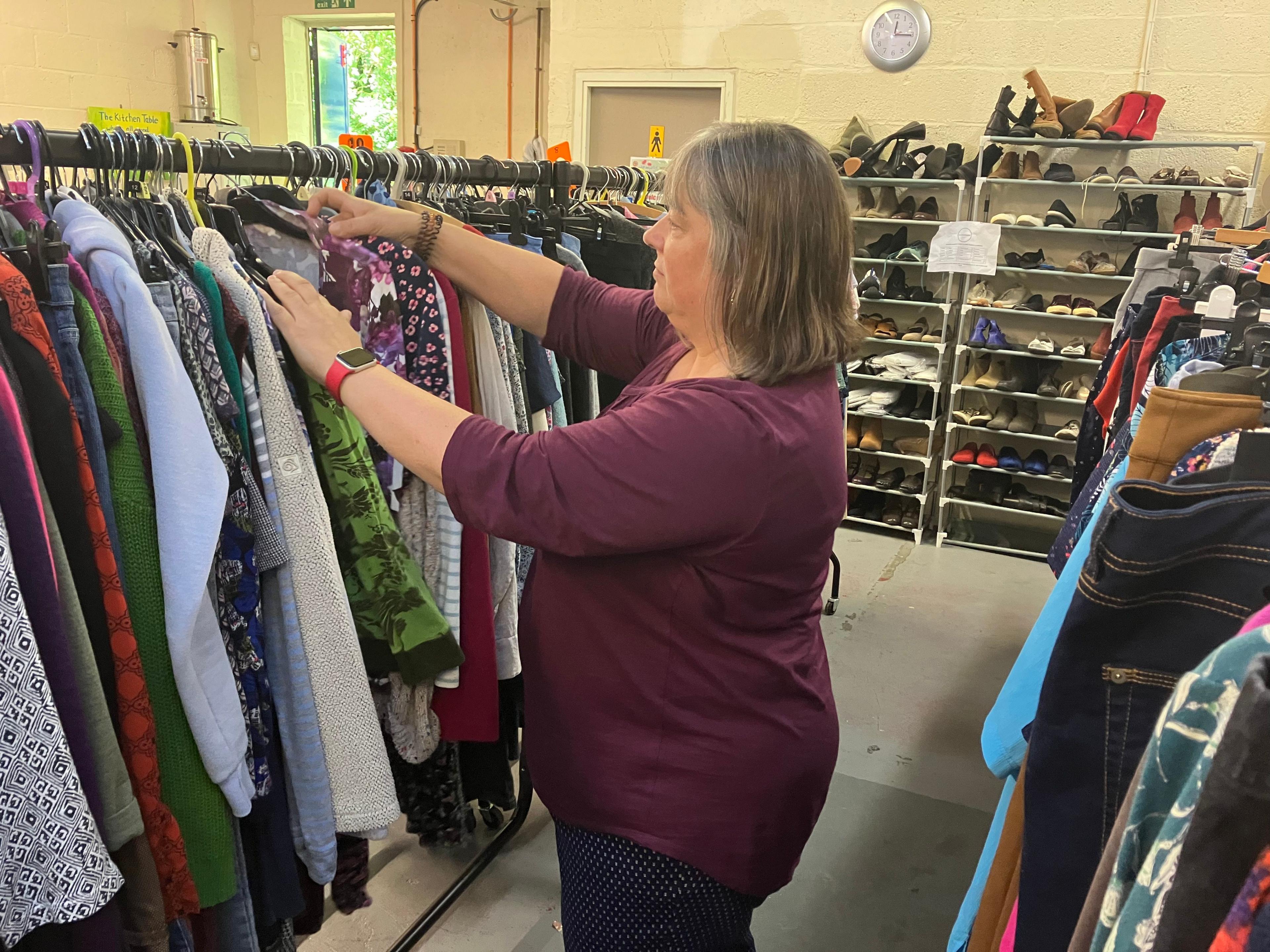 A picture of a woman with a wine-red coloured top and brown hair looking through a selection of clothes on a hanger.