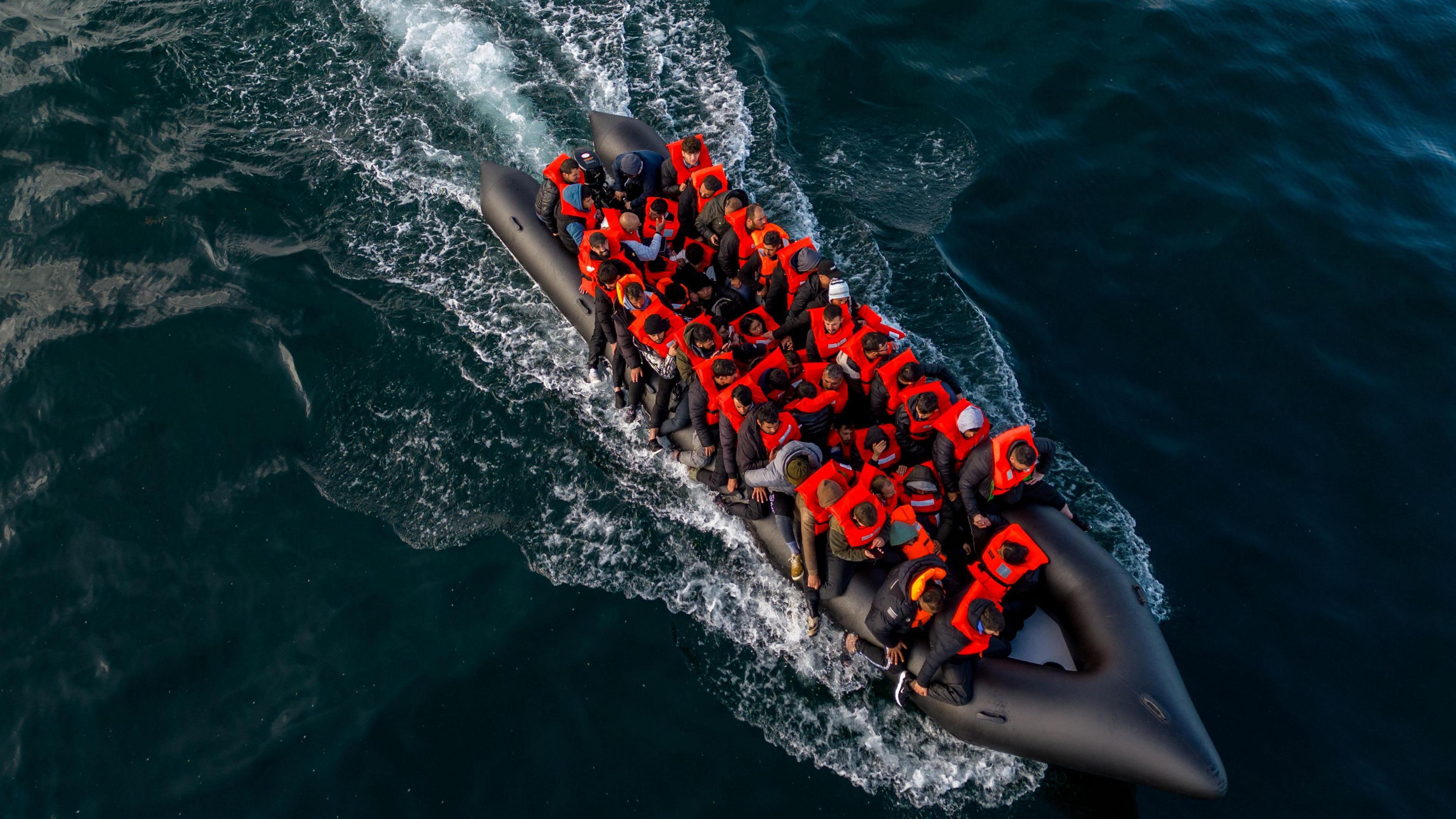 An aerial shot of an inflatable dinghy full of people wearing orange life jackets crossing the English Channel  