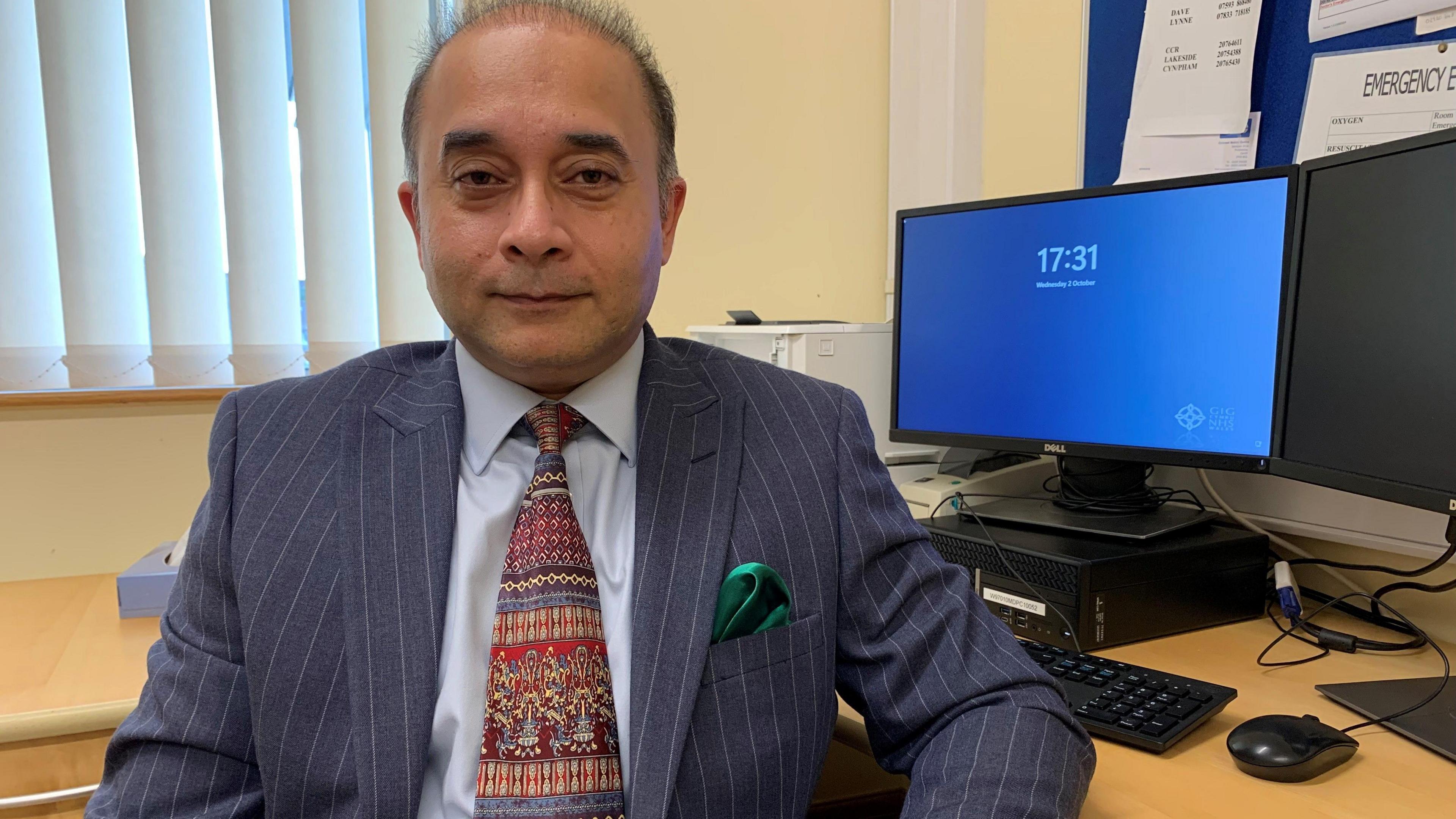 Dr Raman Sakhuja, a consultant psychiatrist in Cardiff, sits at his desk with a computer screen behind his left shoulder