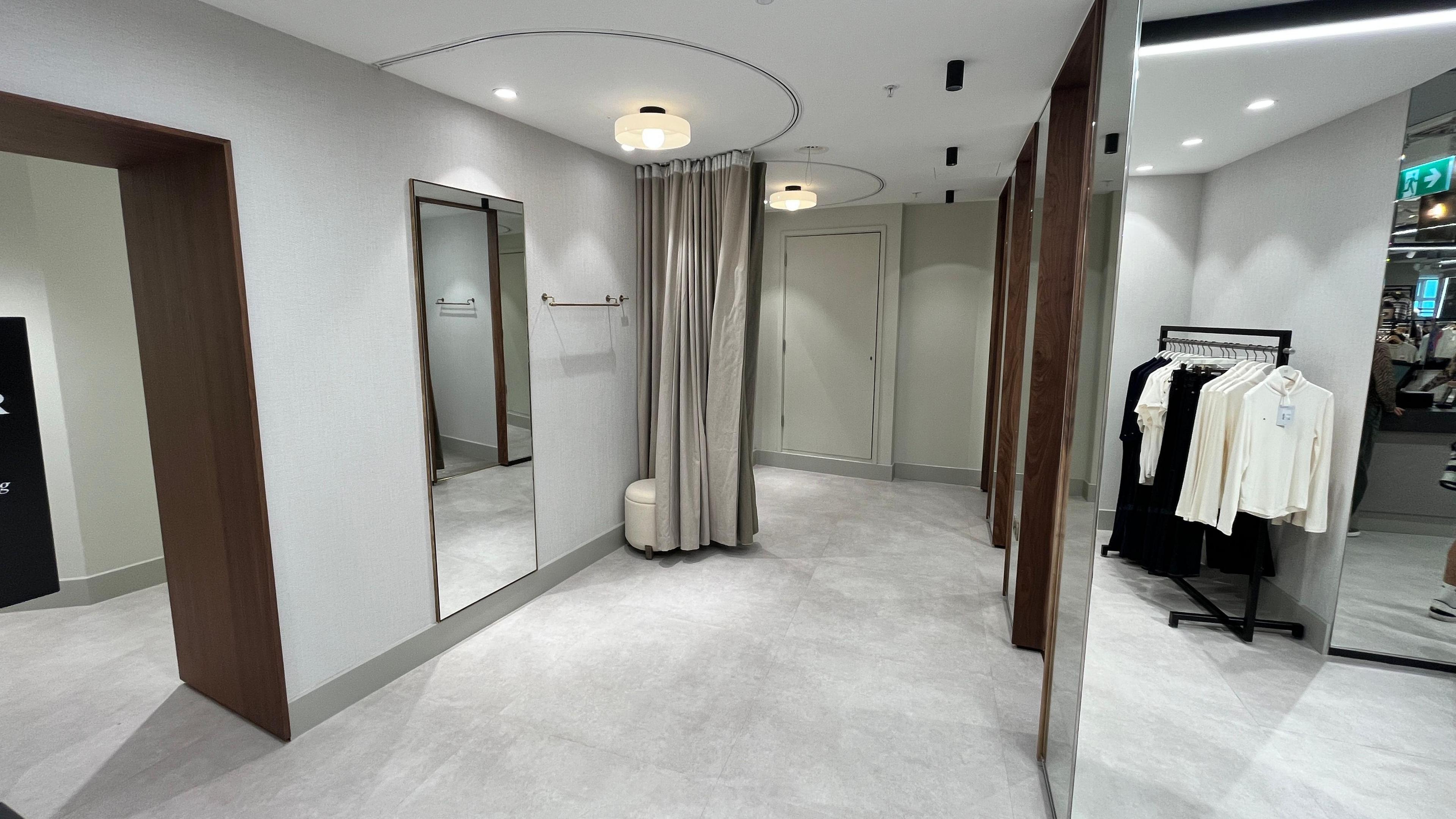 A modern changing room area with stalls, wall to floor mirrors and curtains.