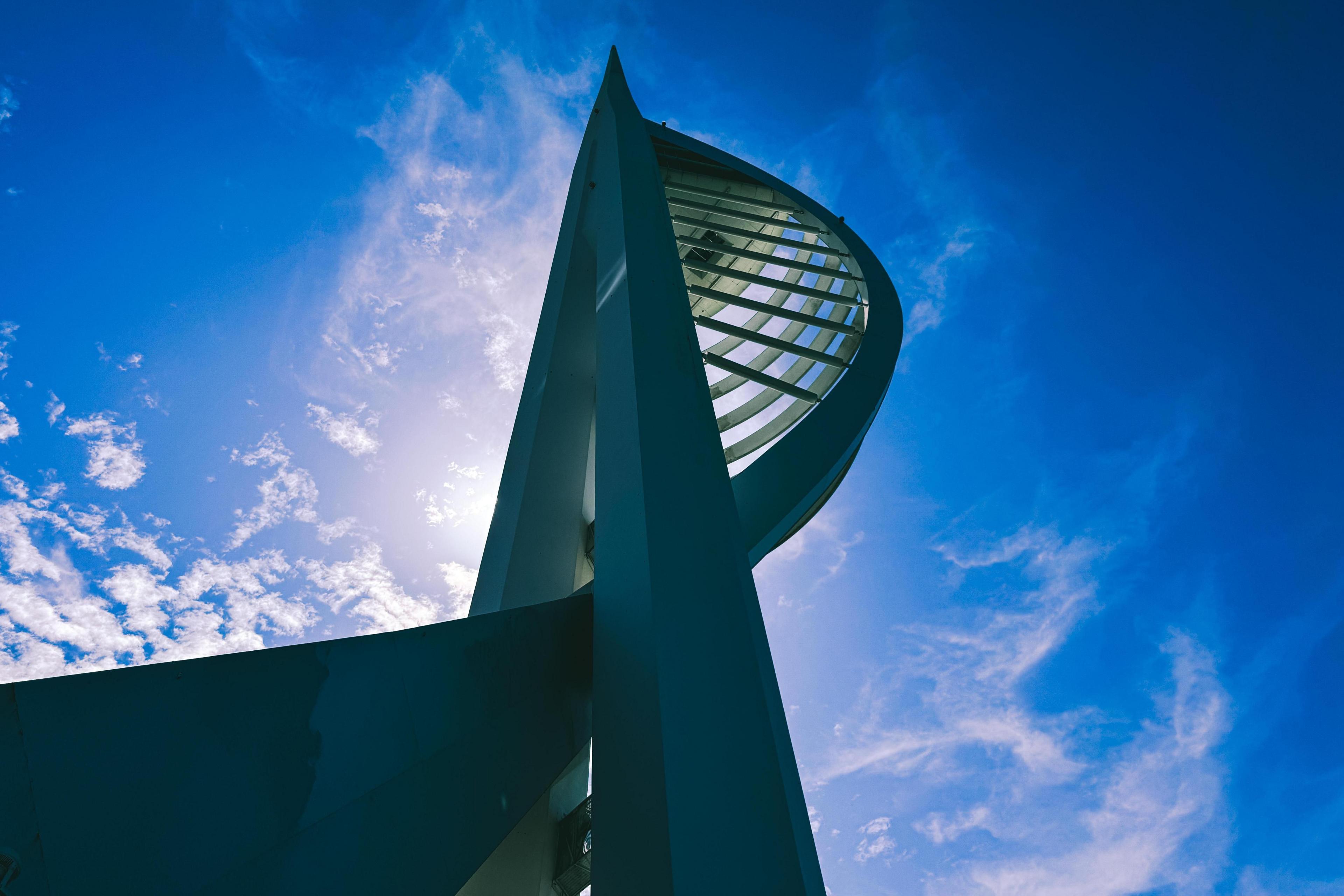 Looking up at the Spinnaker Tower as it is backlit by the sun with blue skies and wispy clouds behind it