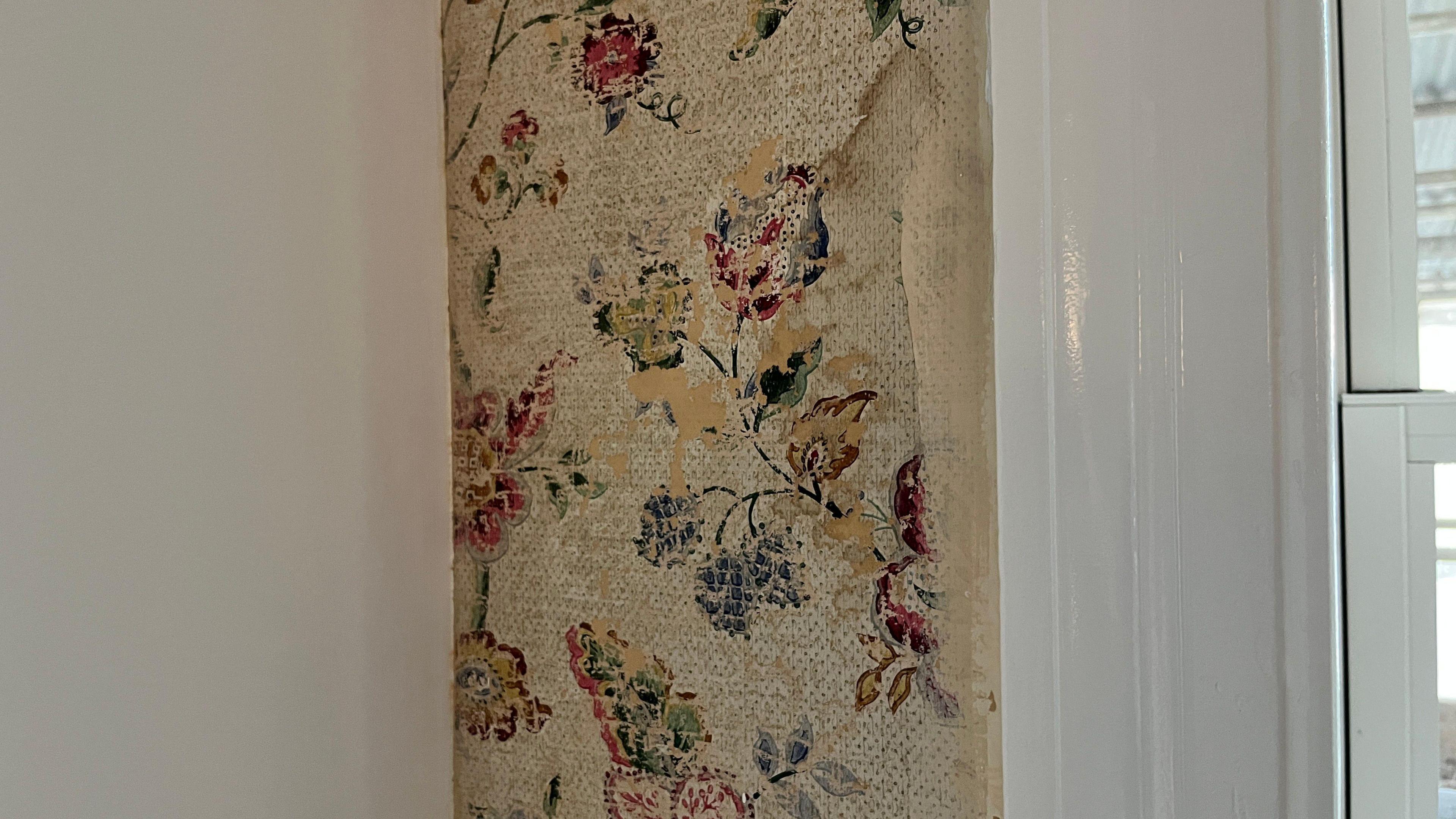 A narrow strip of old wallpaper which is faded in parts. The patter is roses.