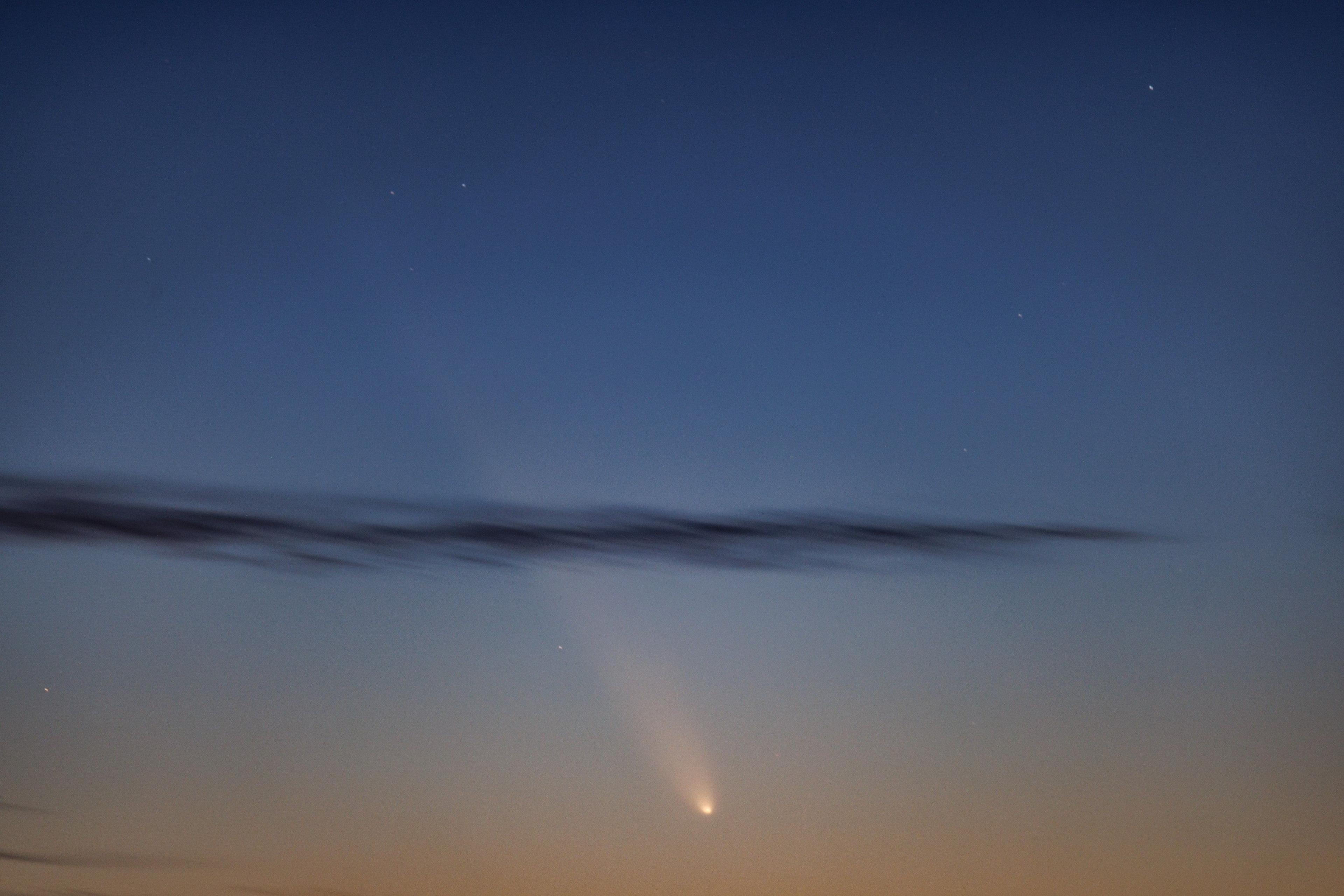 A light night sky with a bright beam of light, with a dark cloud. 