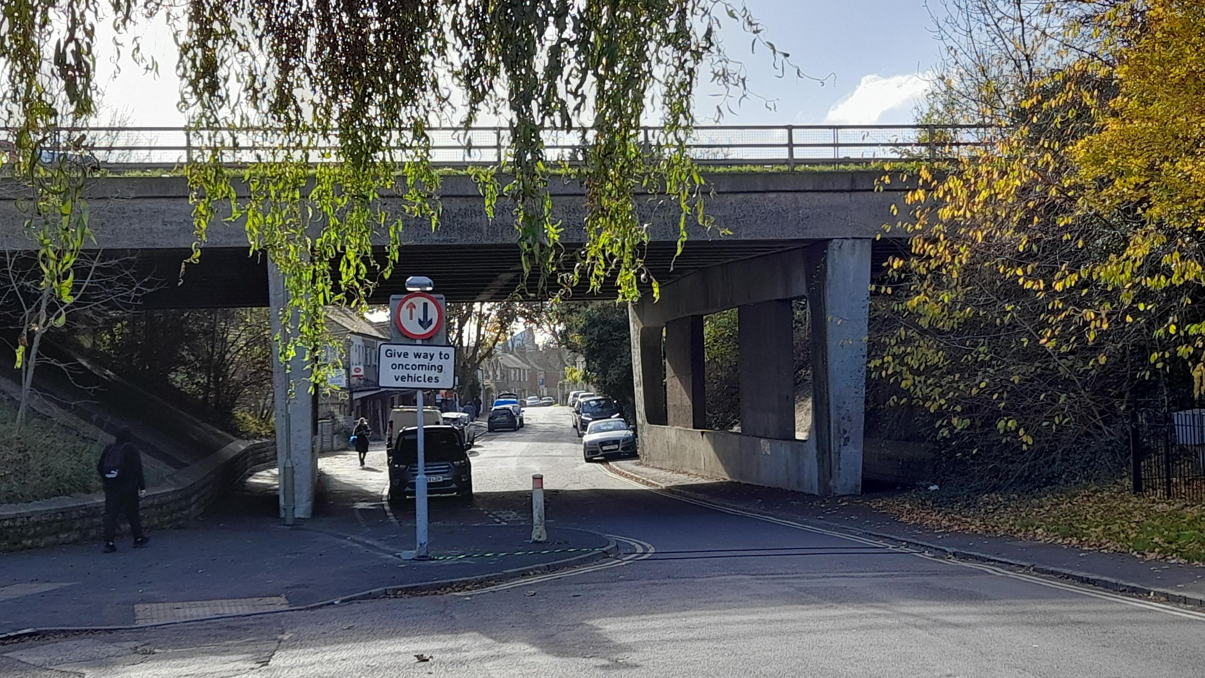 A small road leading to a residential area, with a concrete bridge over it.