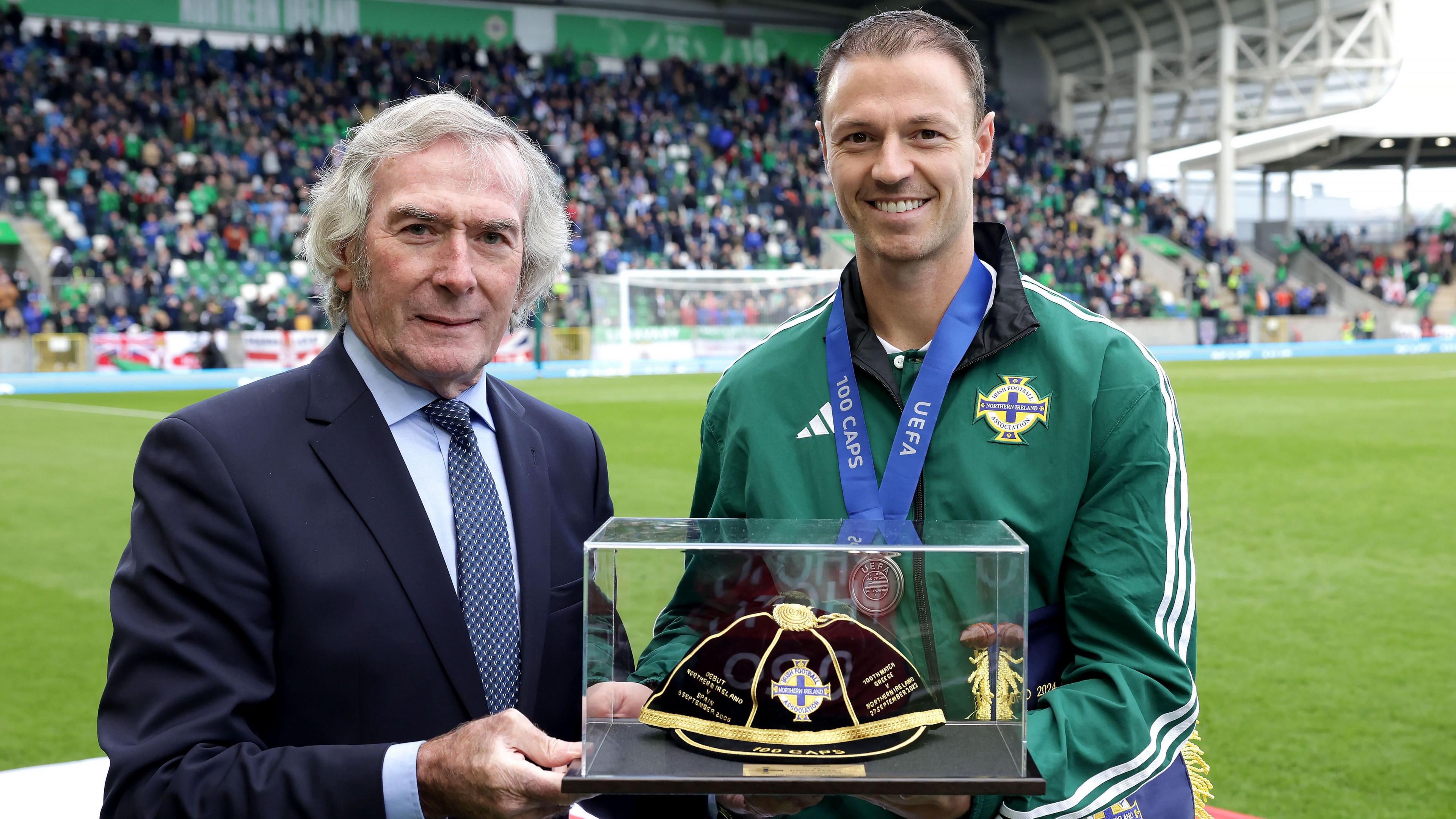 Jonny Evans is presented with a commemorative cap by Pat Jennings