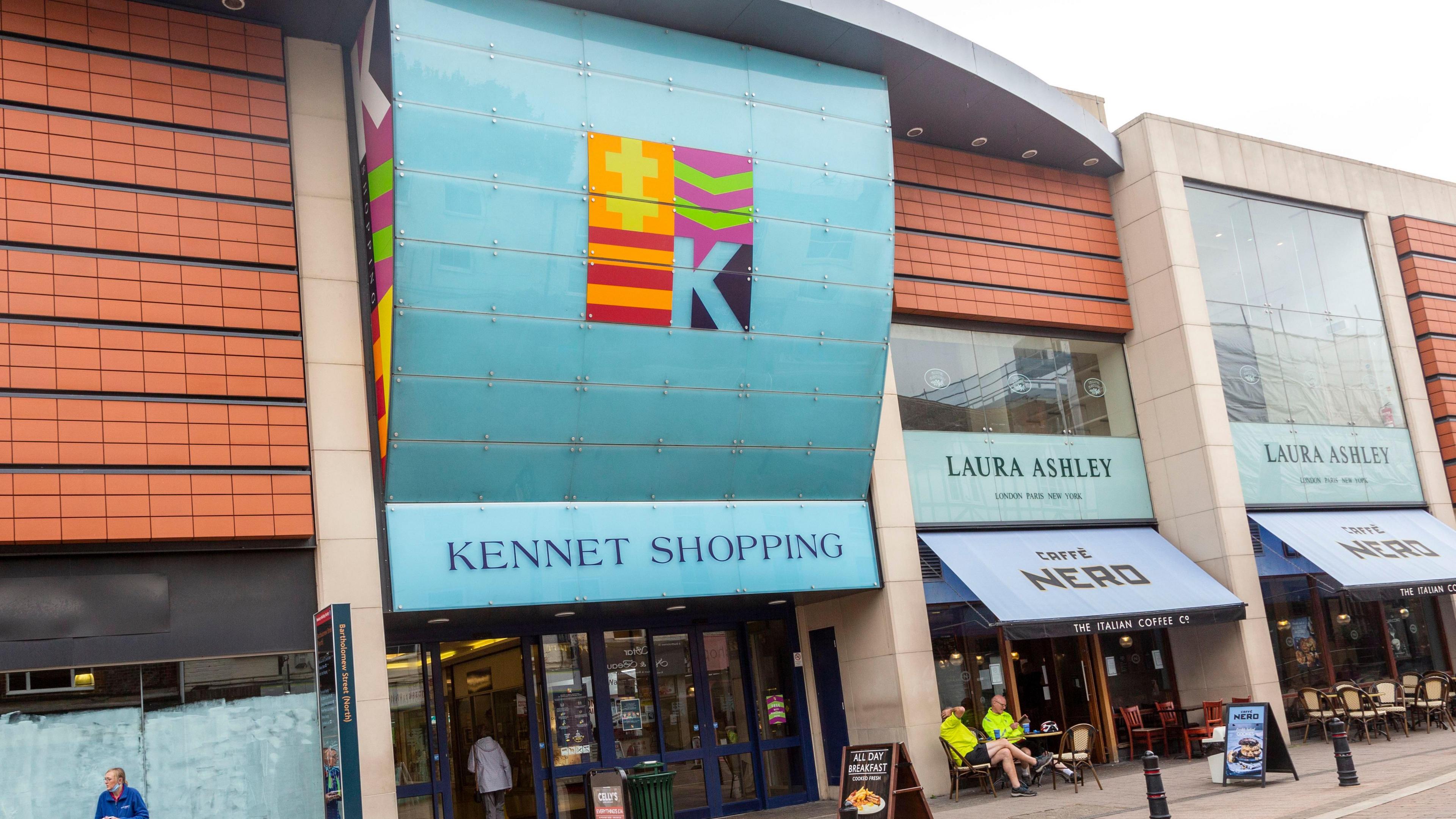 The Kennet Shopping centre on Bartholomew Street in Newbury on an overcast day. Some people are going inside, others are sitting outside Cafe Nero.