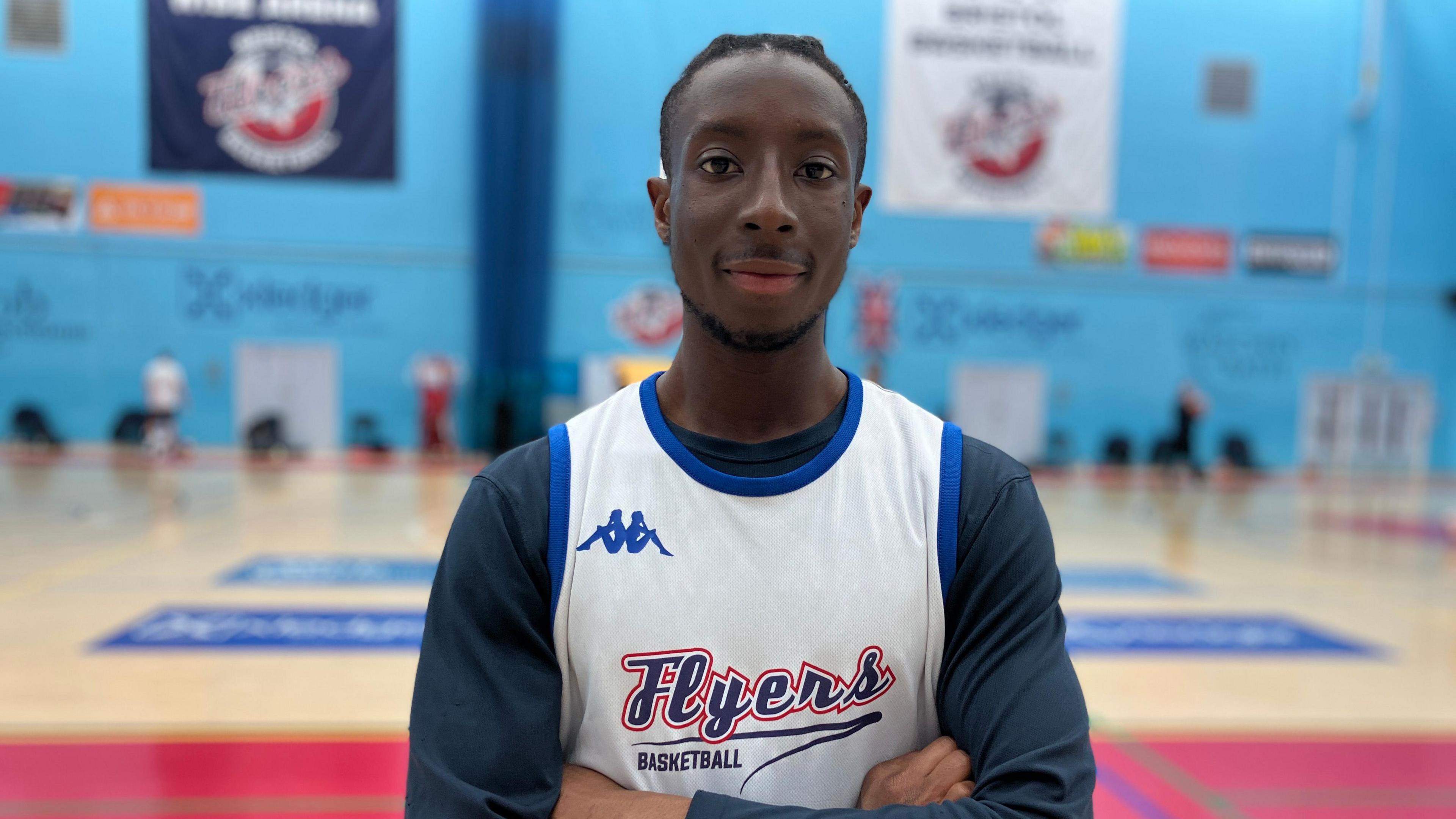 Close-up image of Corey Samuels wearing a Flyers vest with a basketball court in the background.