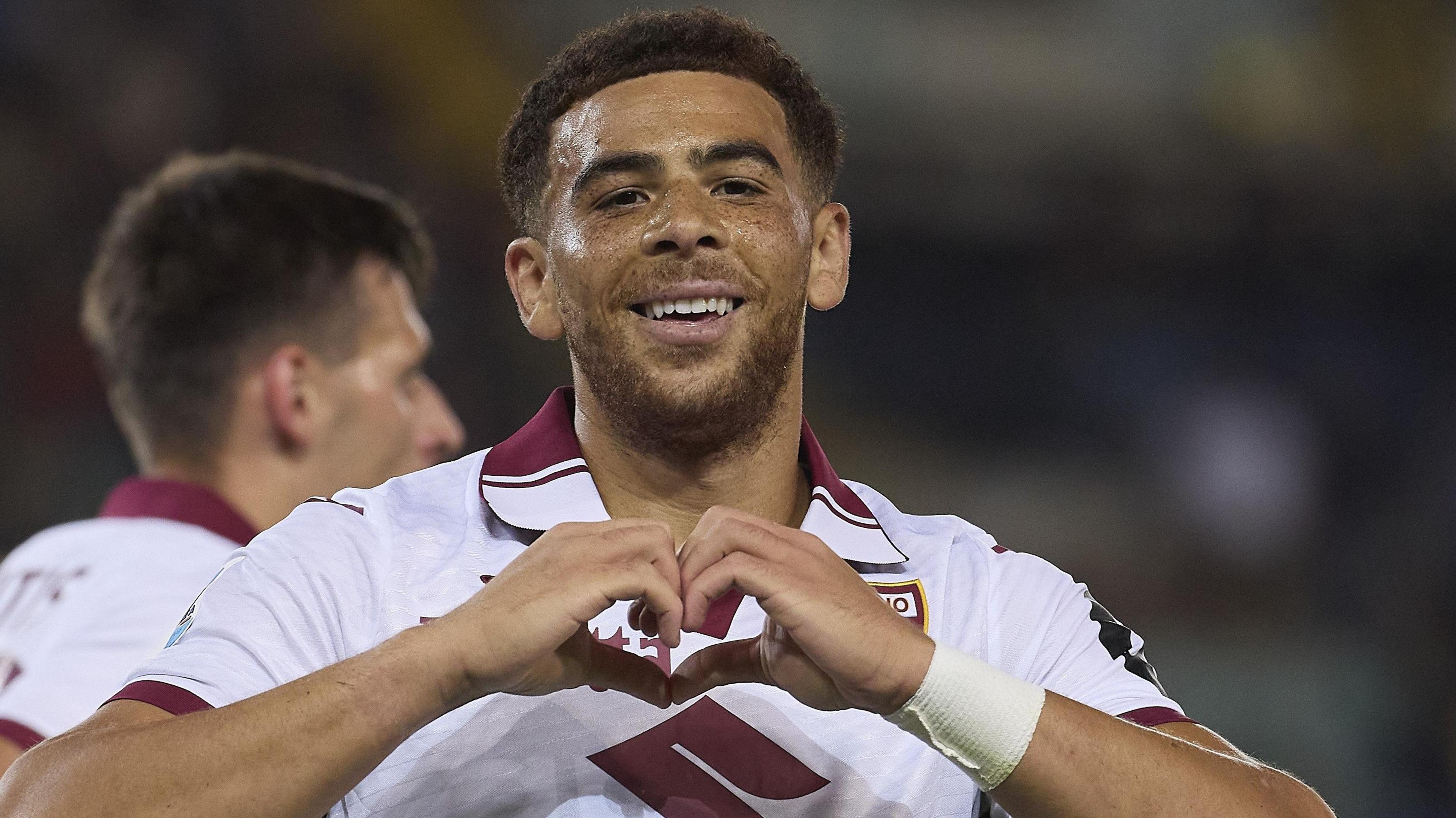 Che Adams looks at the camera and makes a heart shape with his hands while wearing Torino's white and dark red kit. 