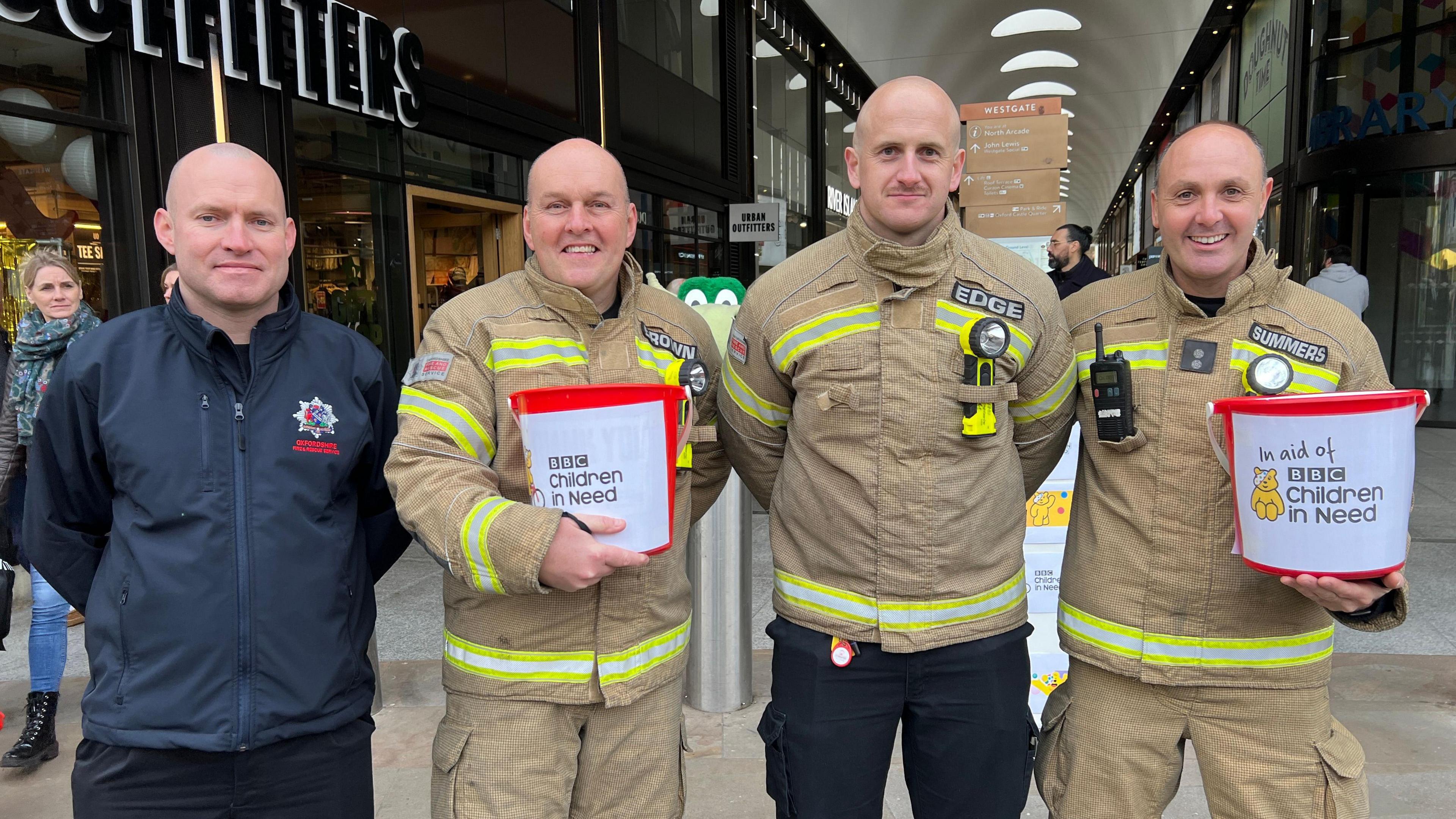 Firefighters stood holding buckets with their arms around each other smiling at the camera