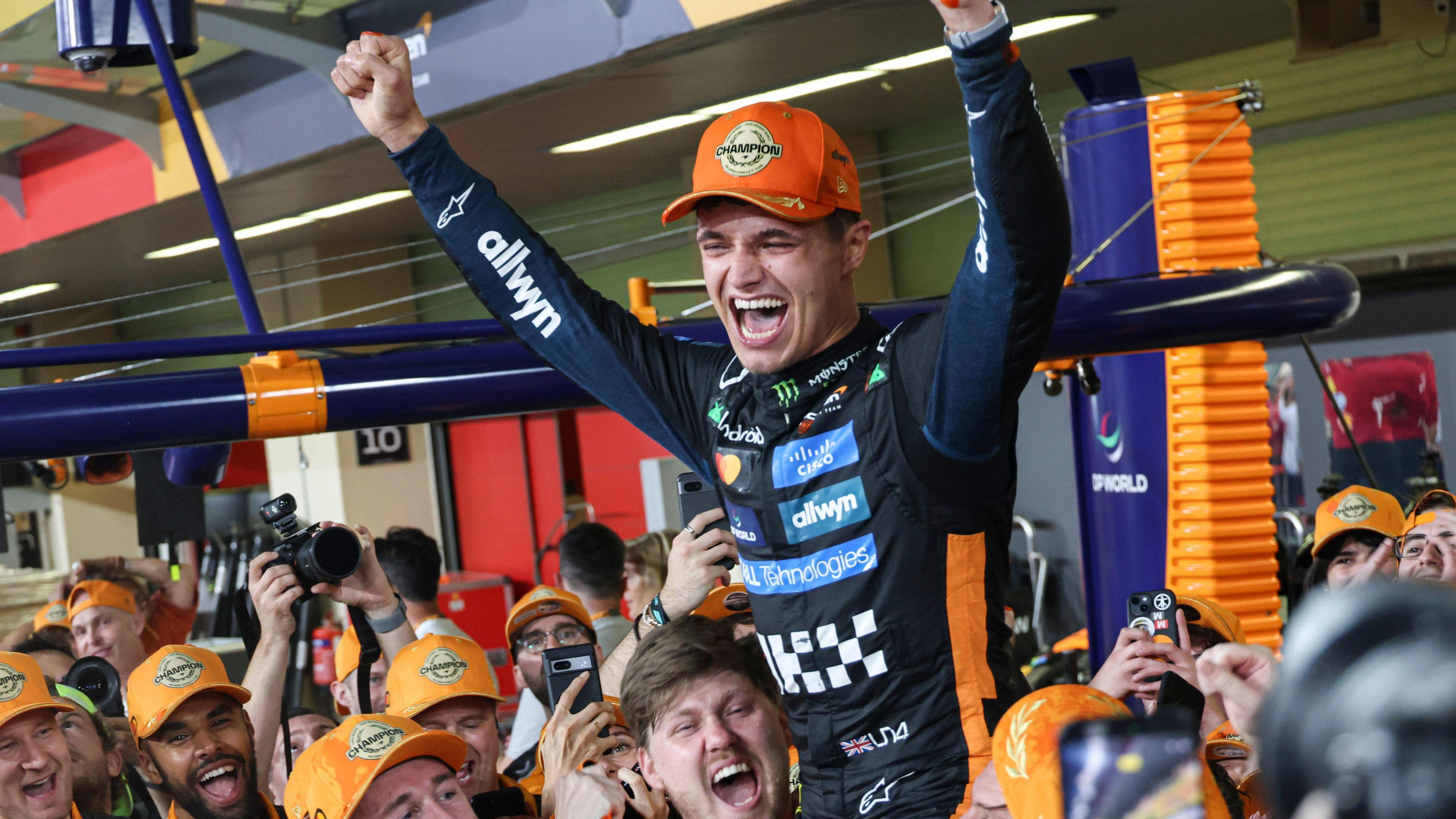 Lando Norris celebrating and held aloft by his team after winning a race.