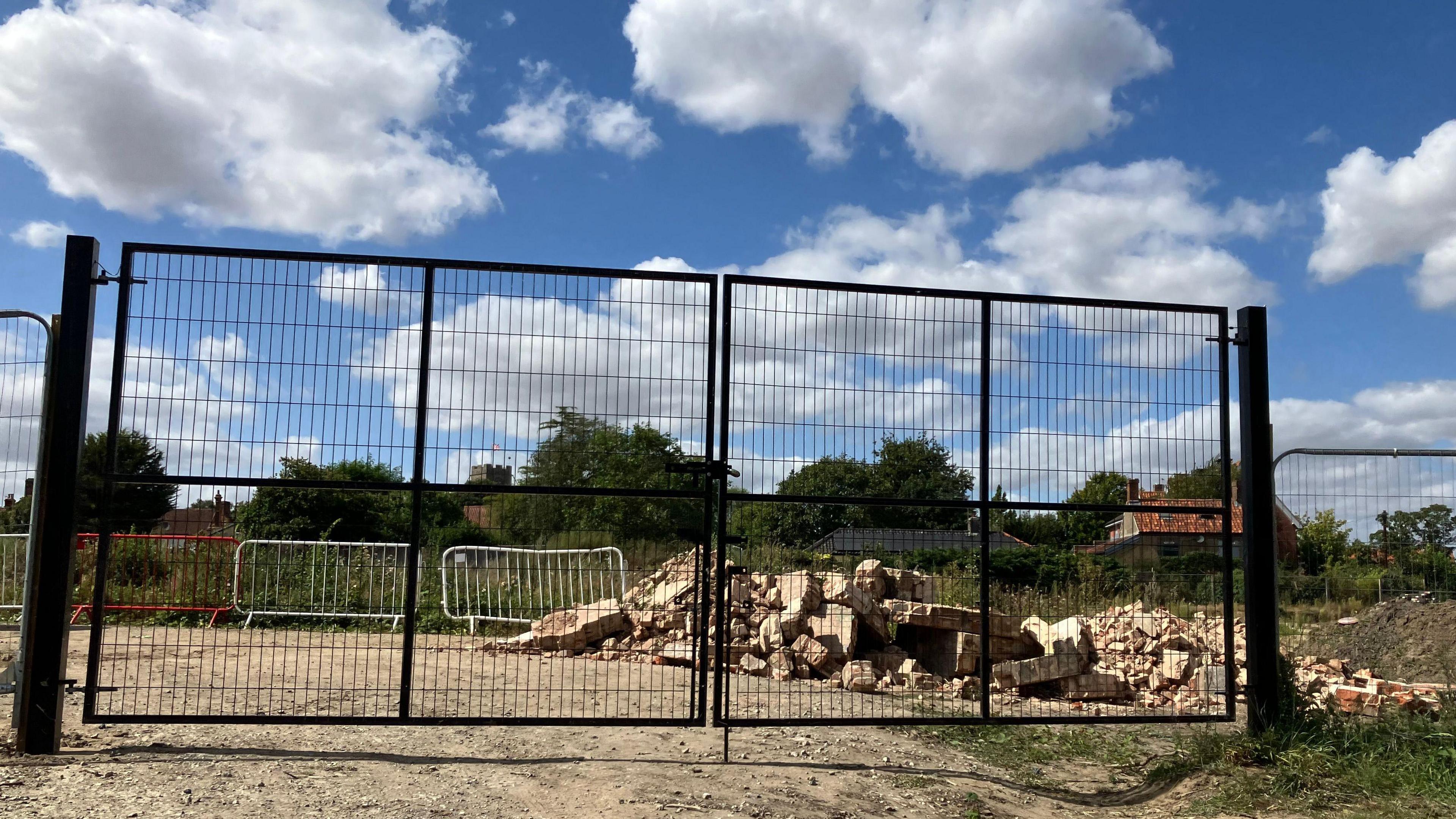 Large, black metal gates are closed and a big pile of rubble can be seen behind them on a building site  