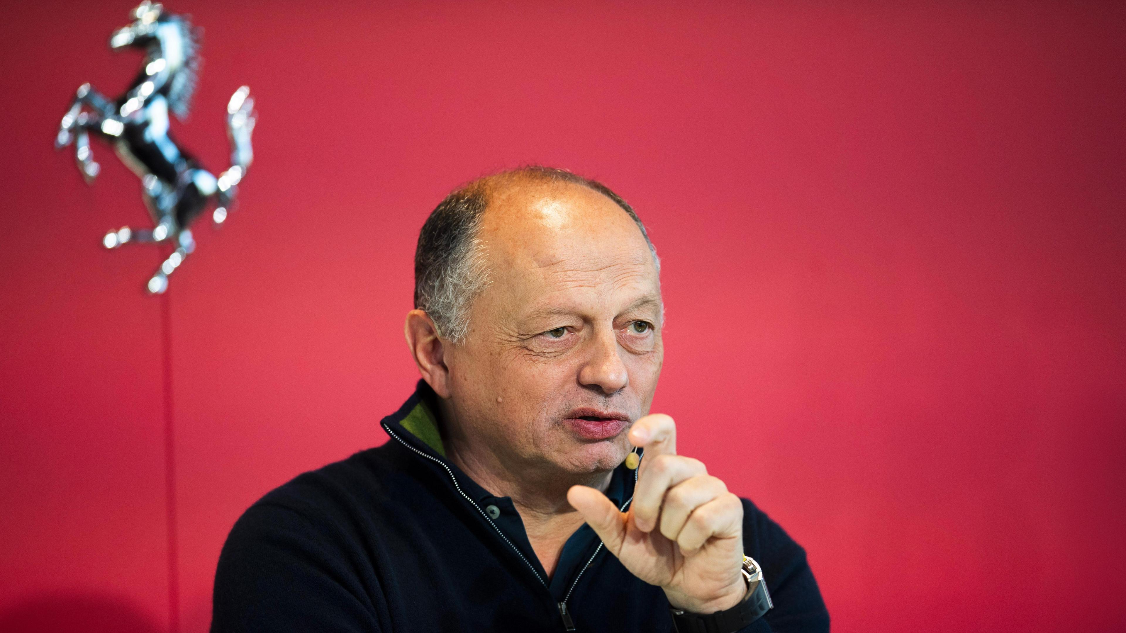 Ferrari team principal Frederic Vasseur in front of a red wall containing a silver Prancing Horse mural