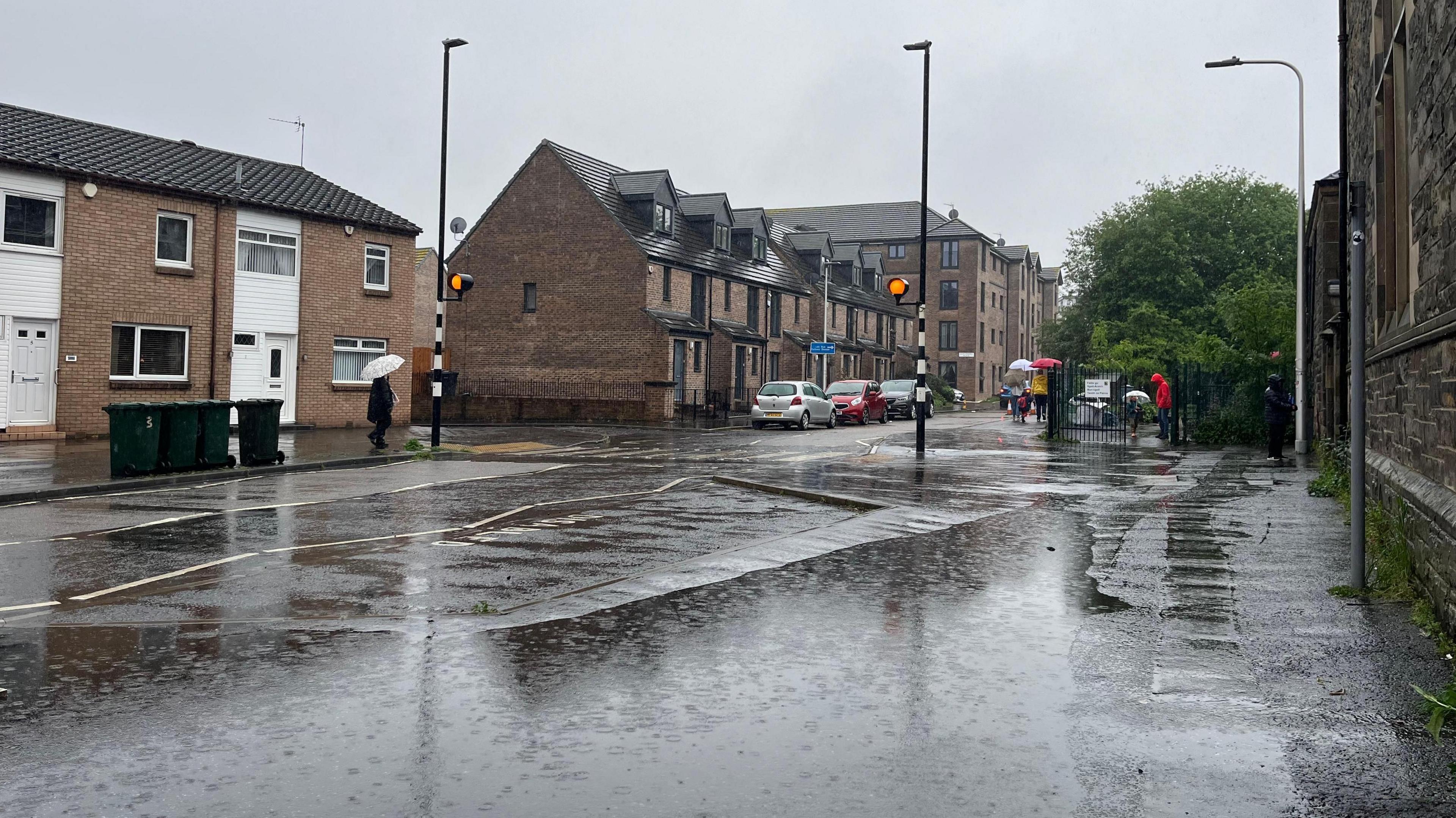 A street scene with rain pouring down and people holding umbrellas in the distance