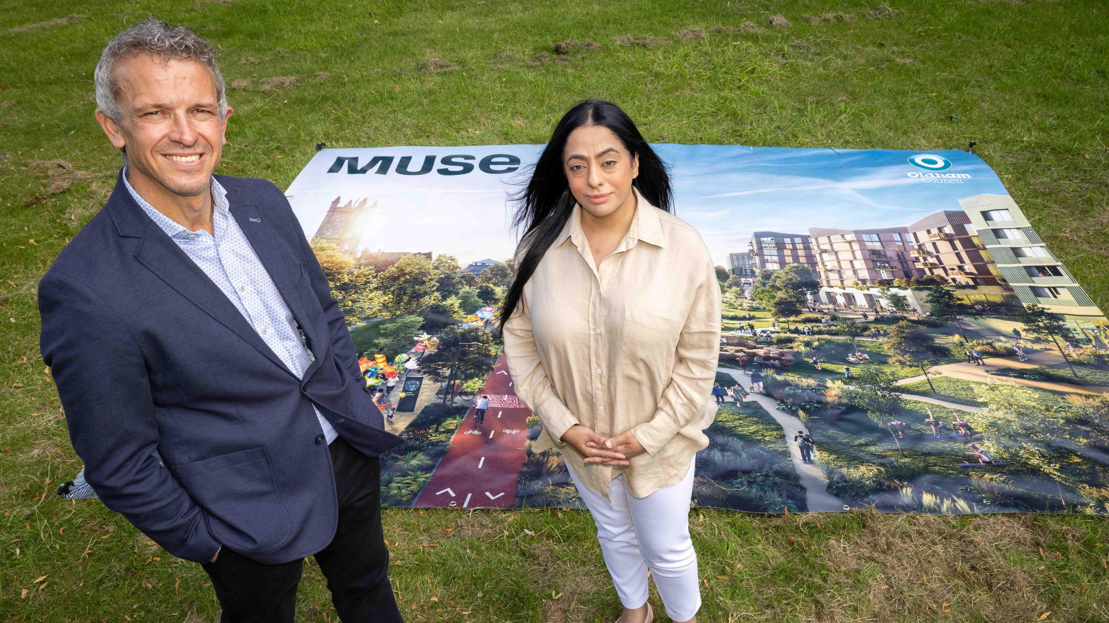 Muse Managing Director Phil Mayall And Oldham Council Leader Cllr Arooj Shah standing in front of a poster that shows the artist's impression of the cycle and pedestrian paths, leafy green trees and walkways