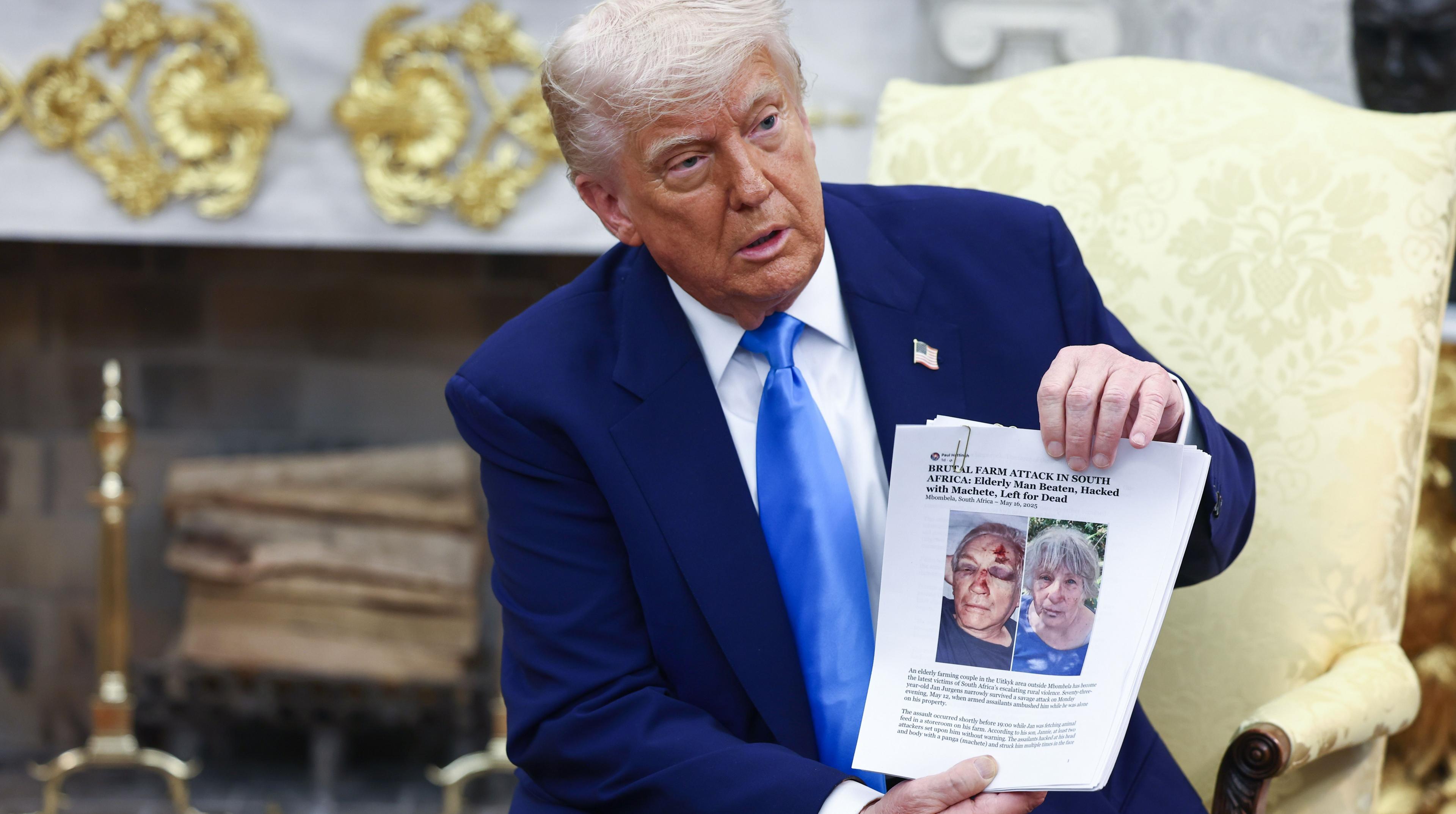 US President Donald Trump holds up news articles related to violence in South Africa