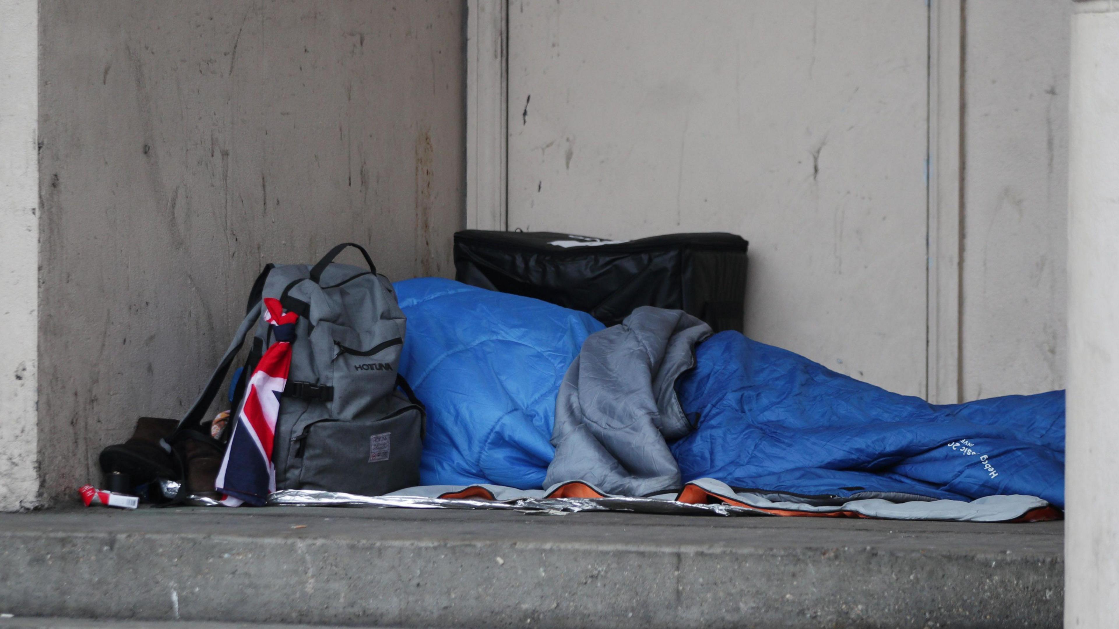 An unidentifiable person in a sleeping bag on the street