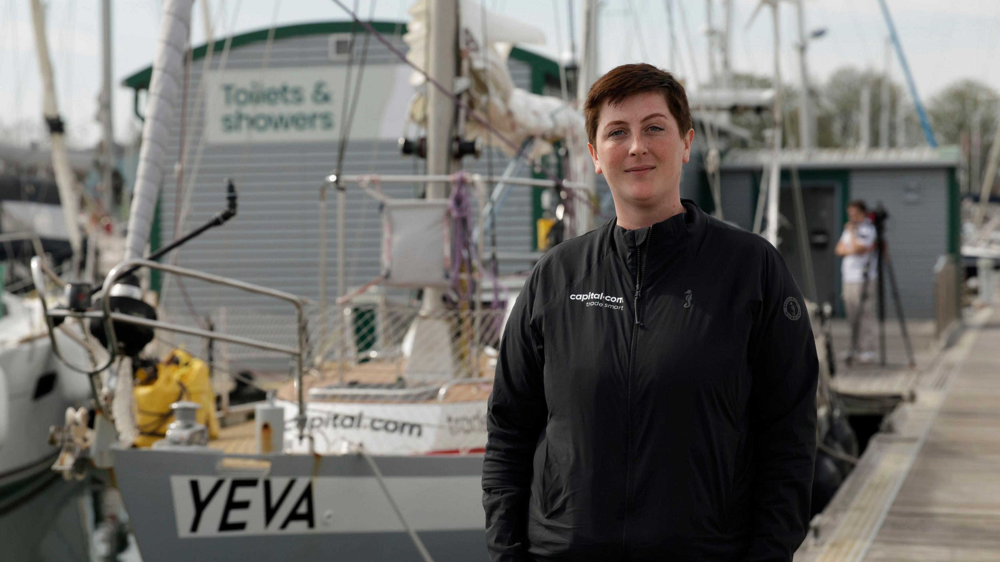 Ella Hibbert wearing all black and stood on the dock in front of her boat