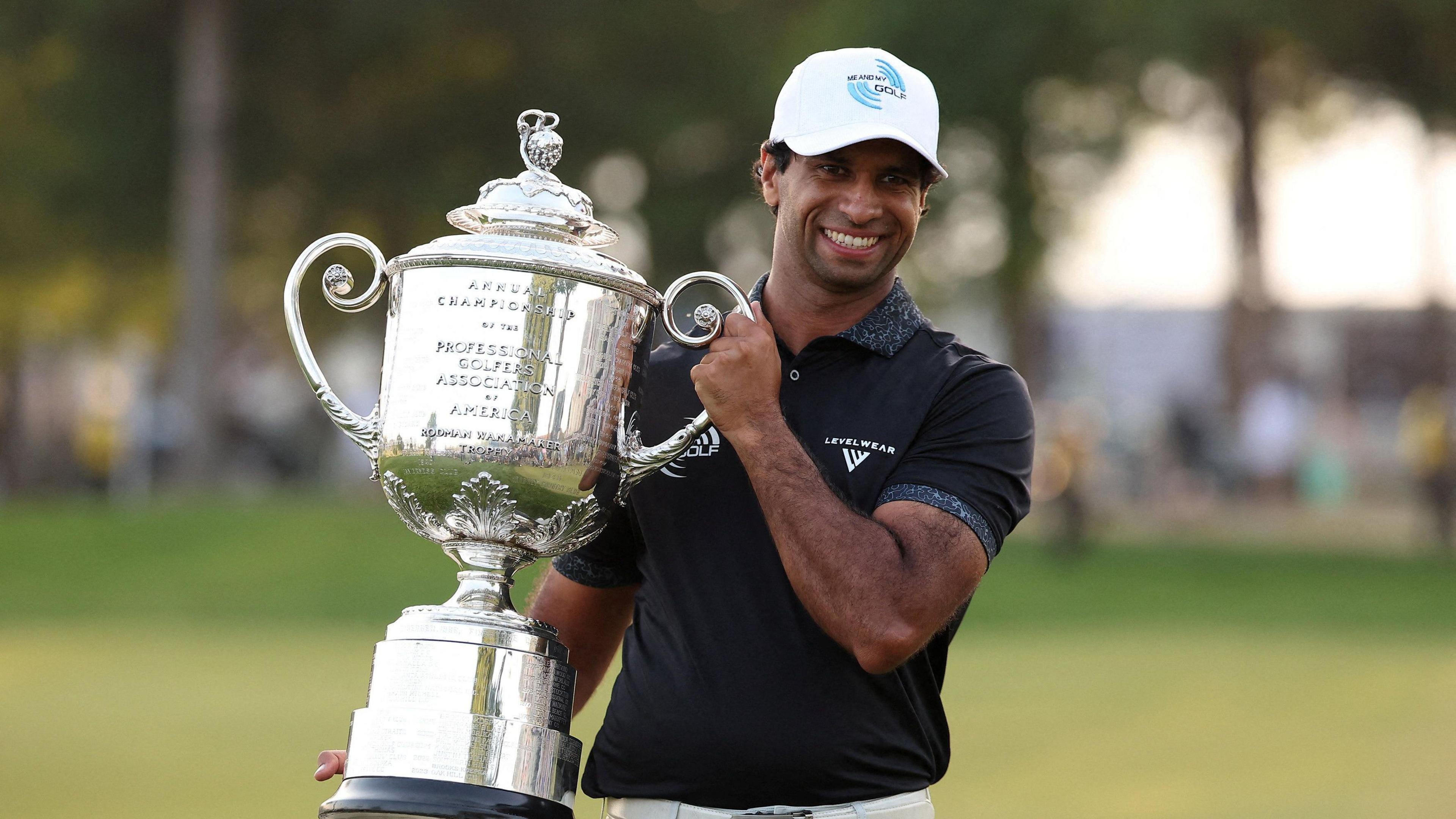 Aaron Rai holding a big trophy and smiling at the camera