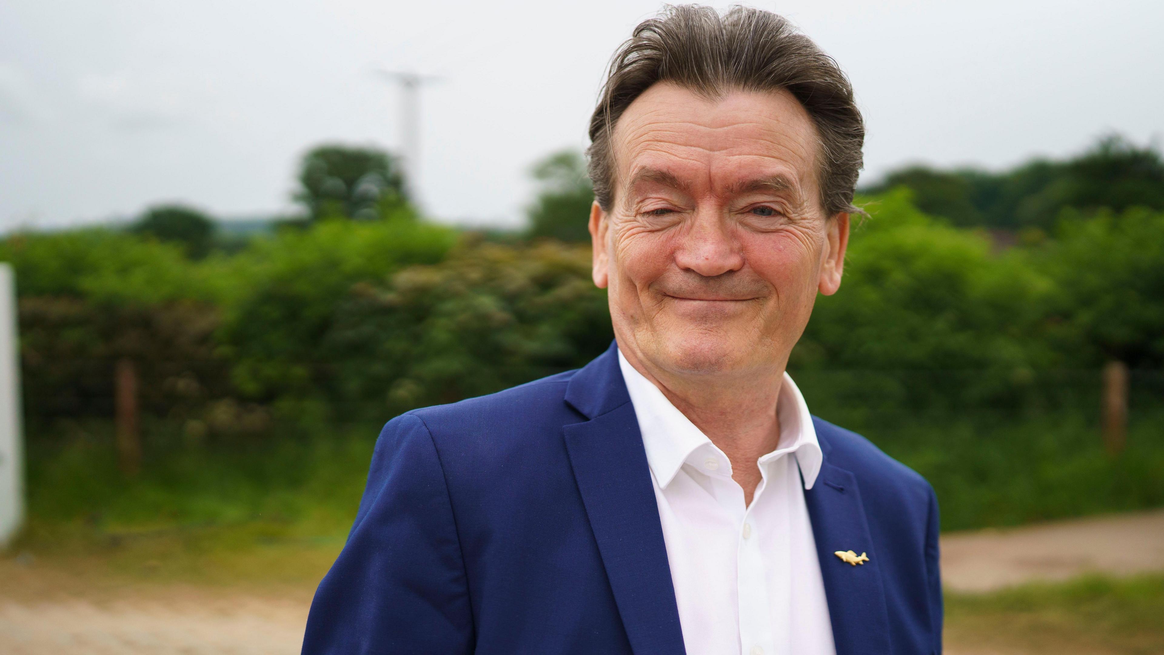 Feargal Sharkey looking at the camera and smiling, he is wearing a blue suit and white shirt.