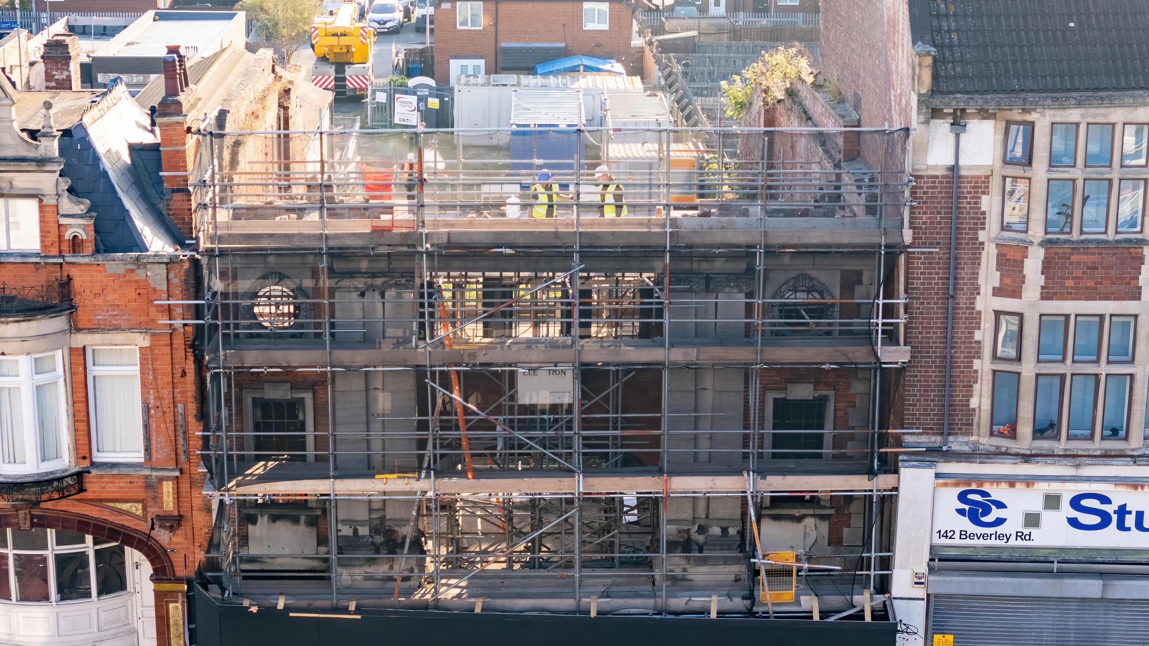 The bombed-out building is covered in scaffolding, with the workers looking at the beam at the very top of the building.