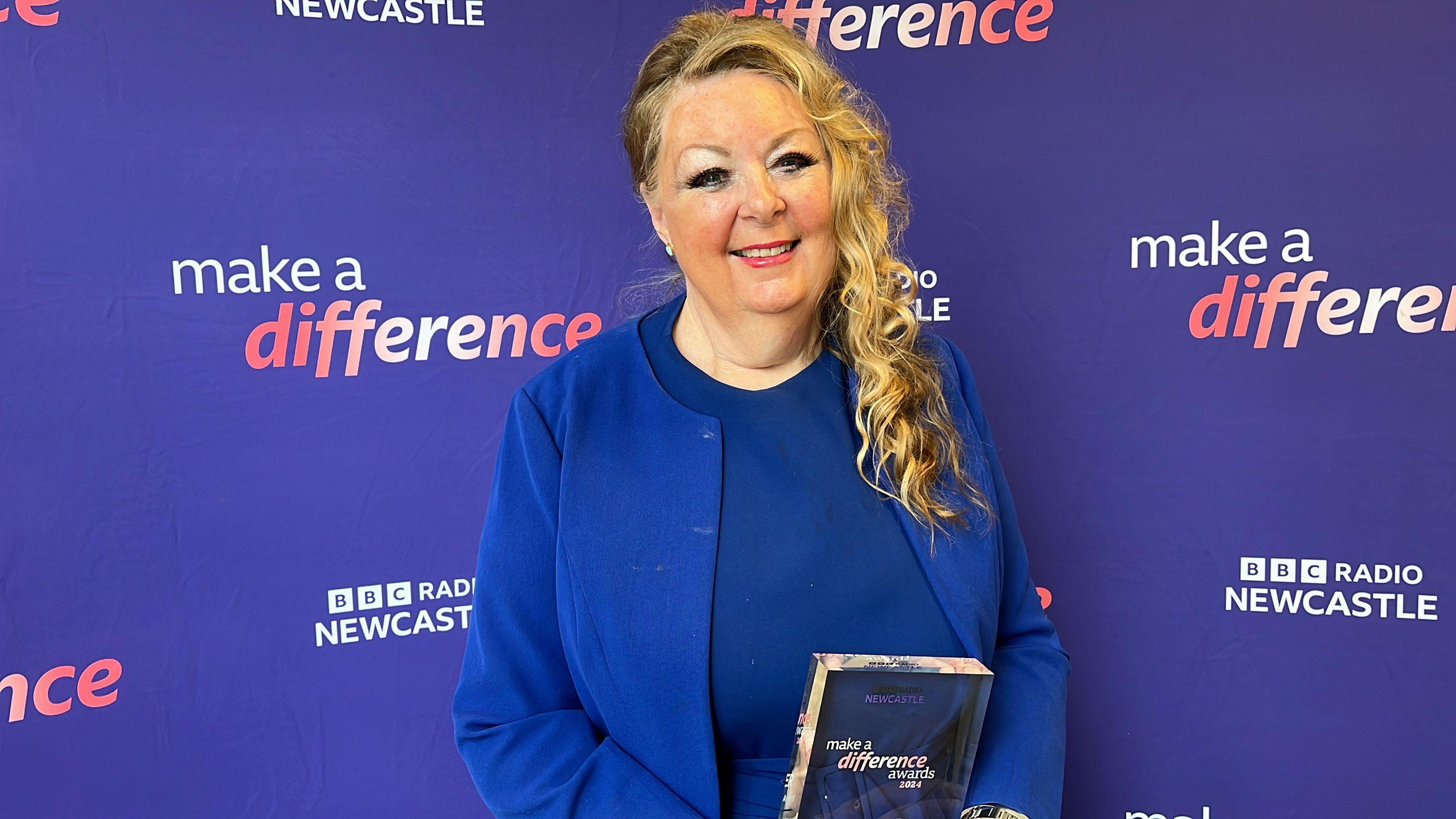 Vivien Watts holding her award. She is wearing a blue outfit.