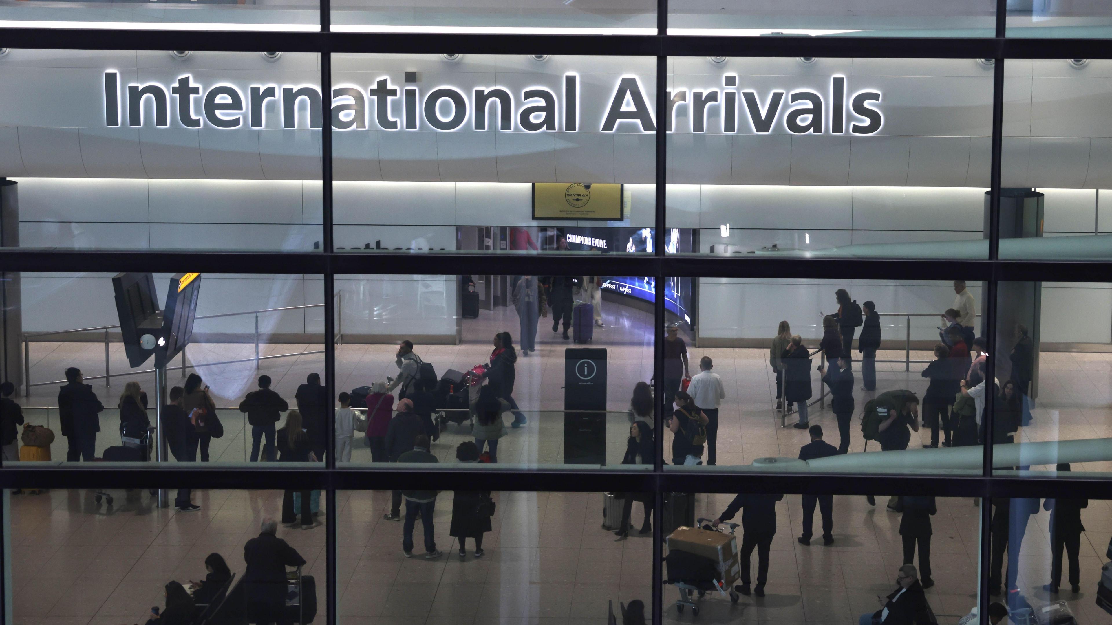 The photo has been taken through a glass window and shows the 'International Arrivals' zone of Heathrow airport