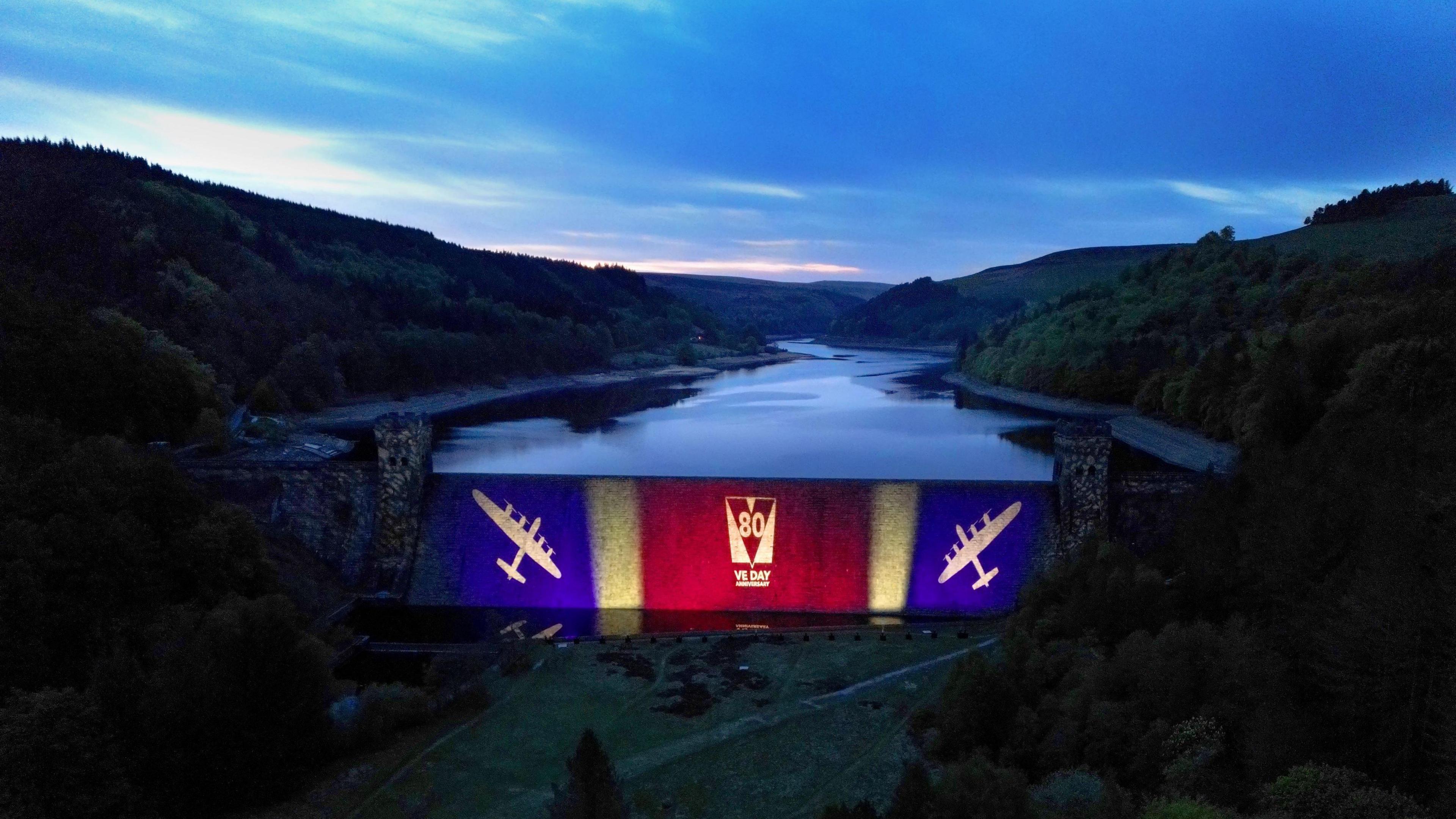 An image of the Derwent dam at night lit up to celebrate 80 years of VE Day in 2023.