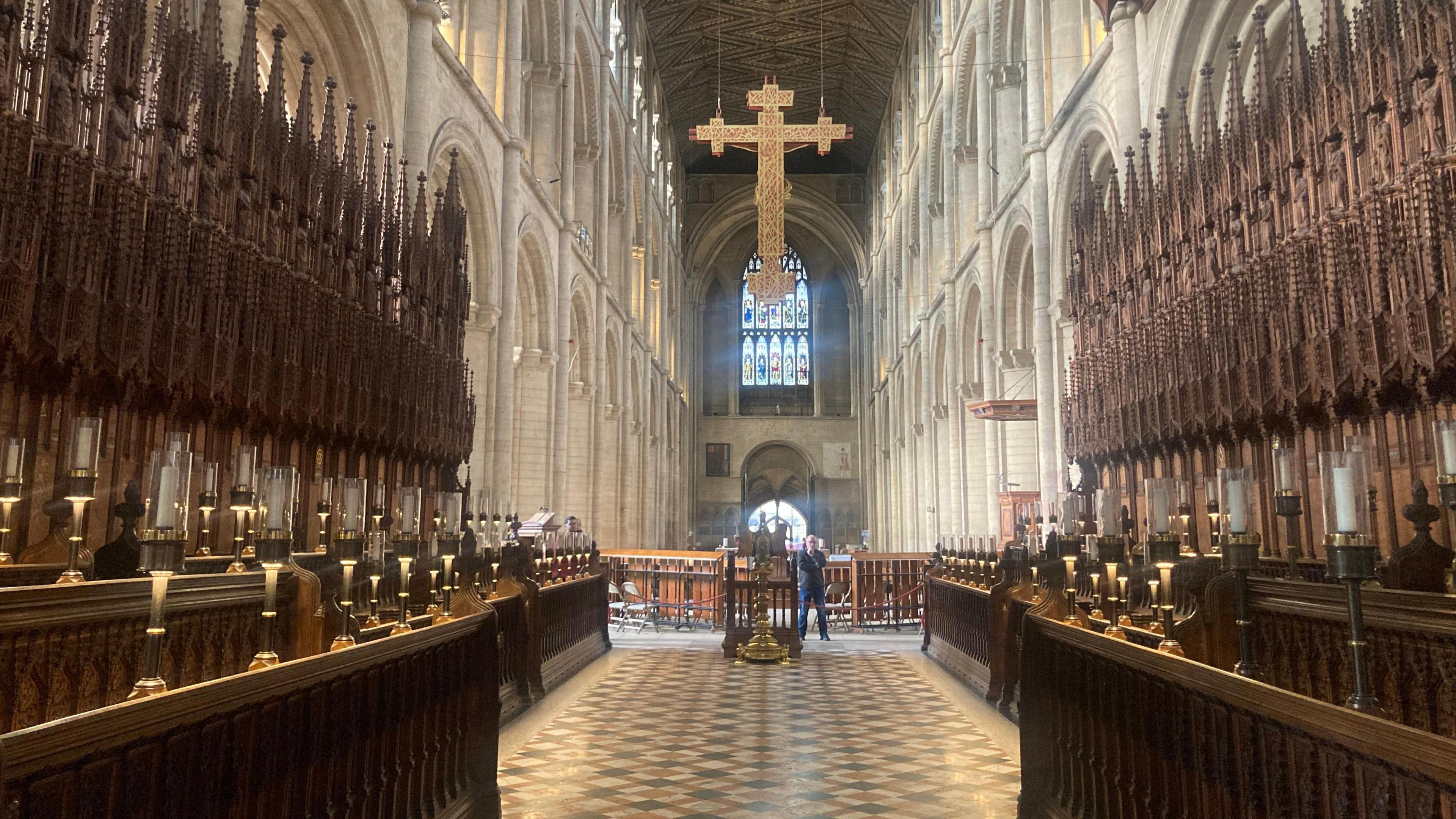 The nave of Peterborough Cathedral, with a big golden cross hanging from the ceiling.