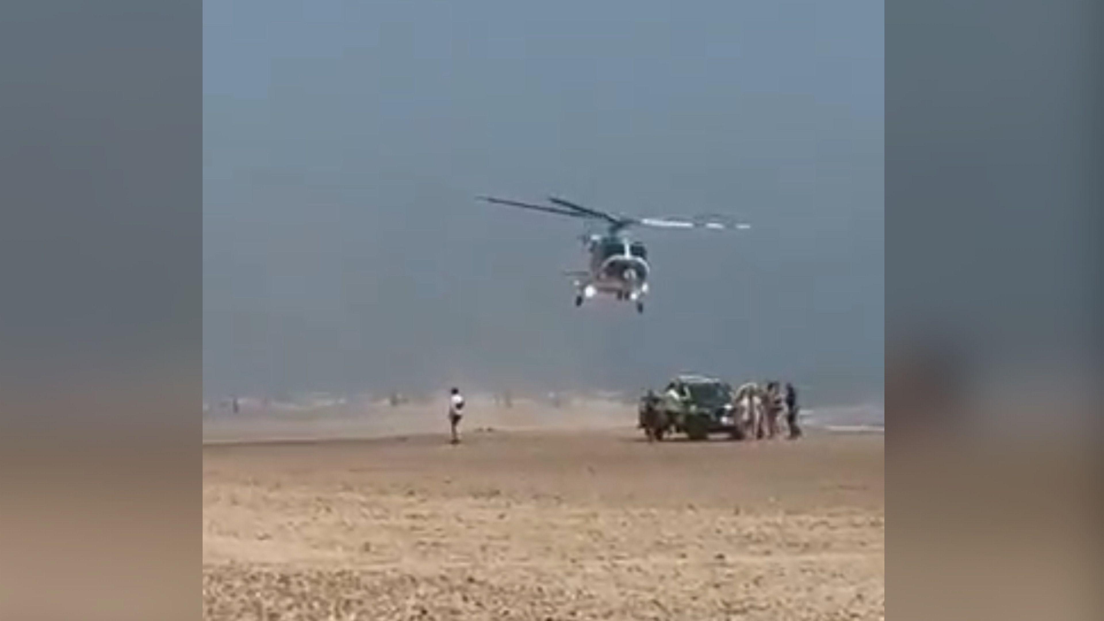 A helicopter lands on a sandy beach. 