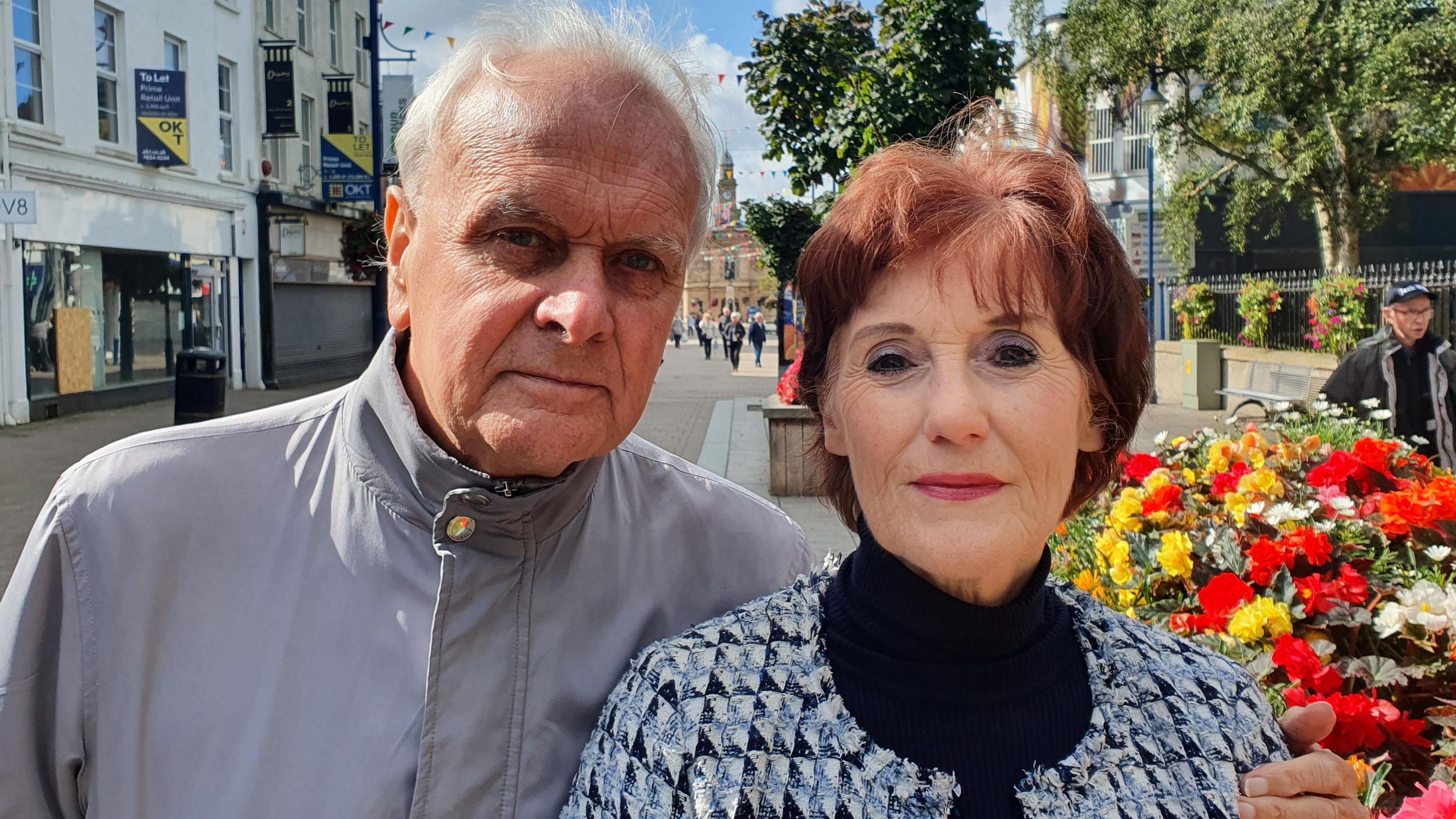 Don McCart and Angela McLaughlin stand together in Coleraine town centre. He is wearing a grey jacket and has his arm around Angela, who is wearing a black top , with a checked jacket. Pedestrians can be seen in the background.