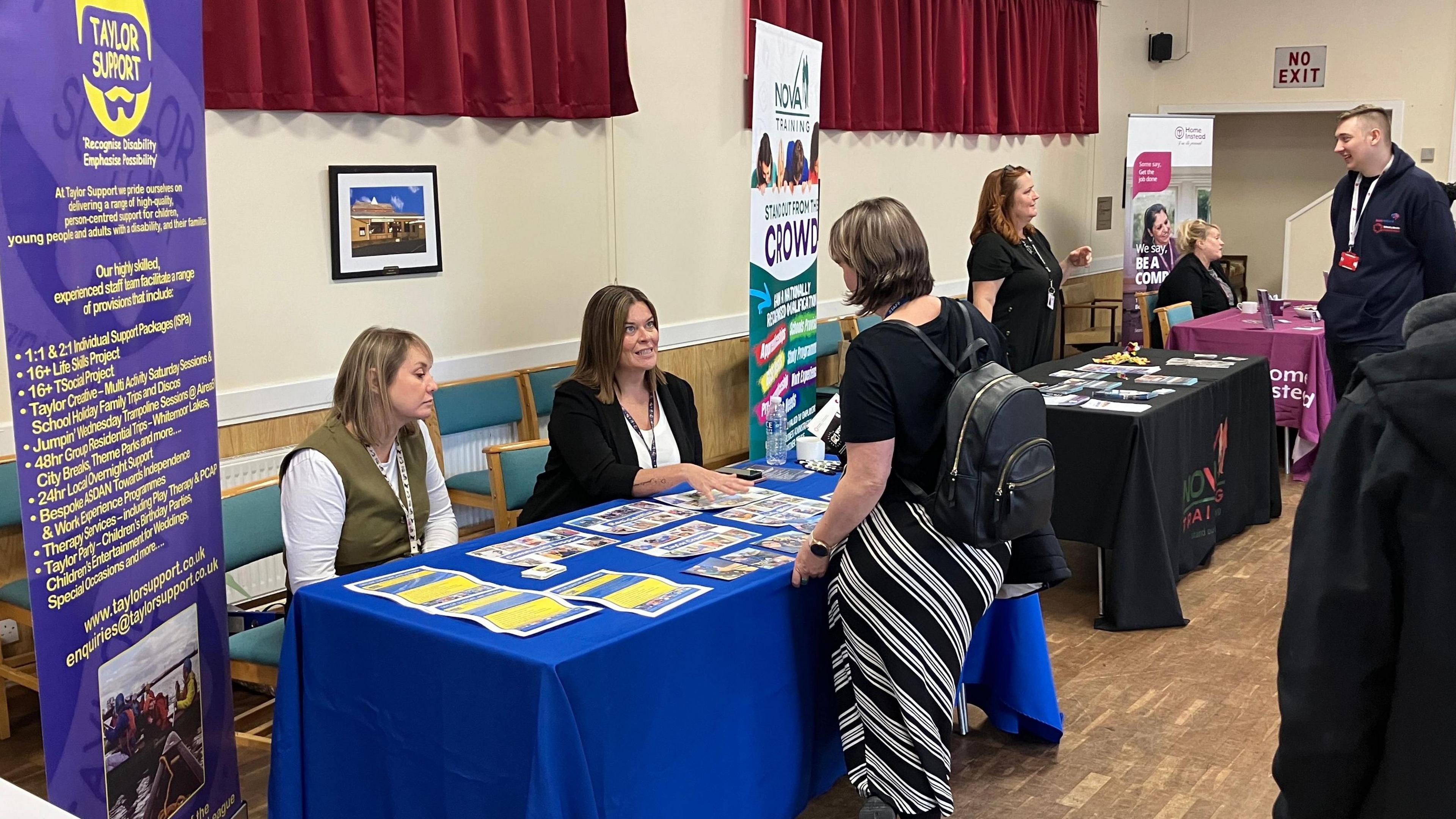 A stall at a jobs fair, with recruiters one side of a blue table and a job seeker the other.