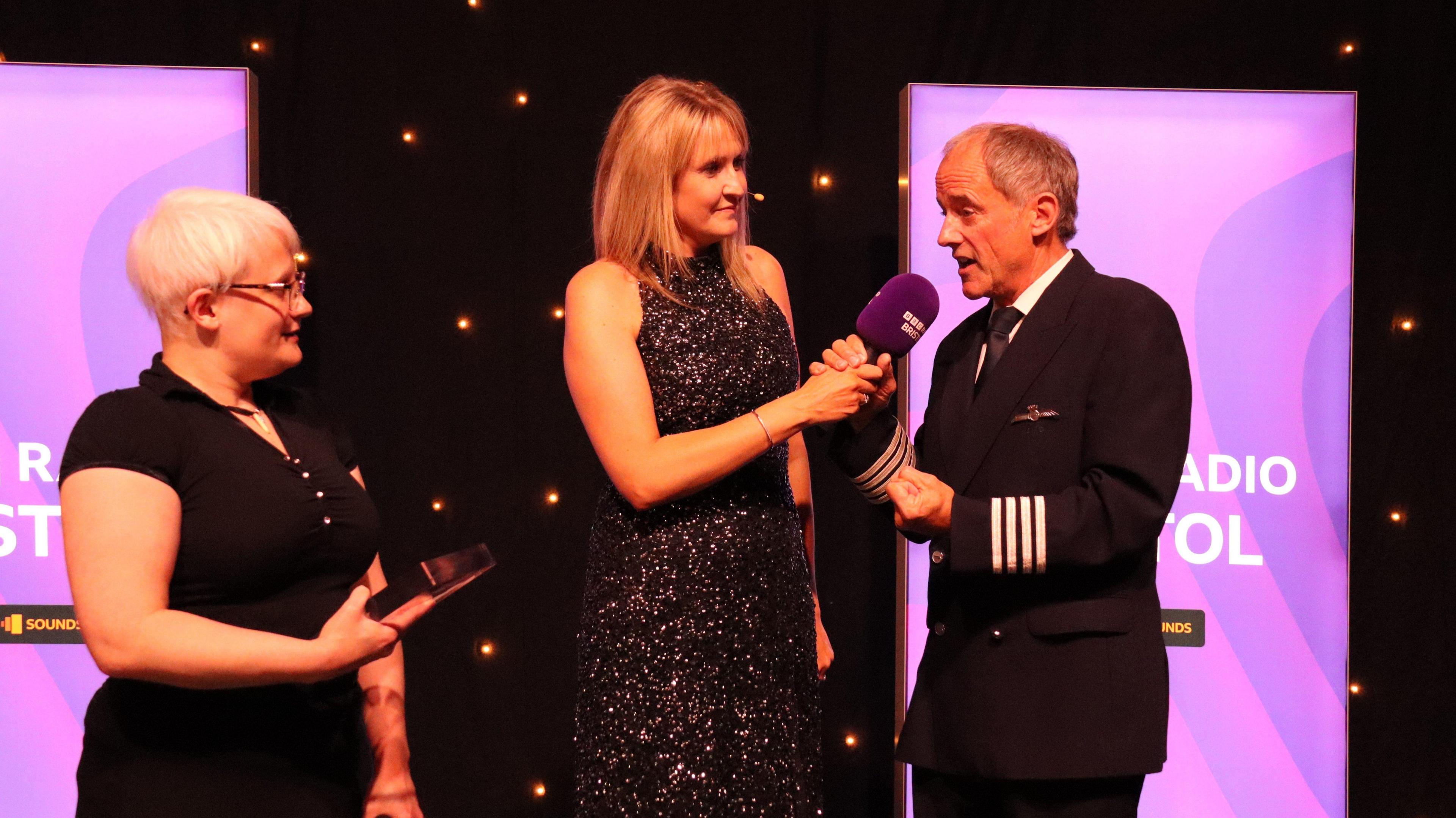 Kim Edwards, Claire Carter and former Concorde captain John Tye standing on a stage.