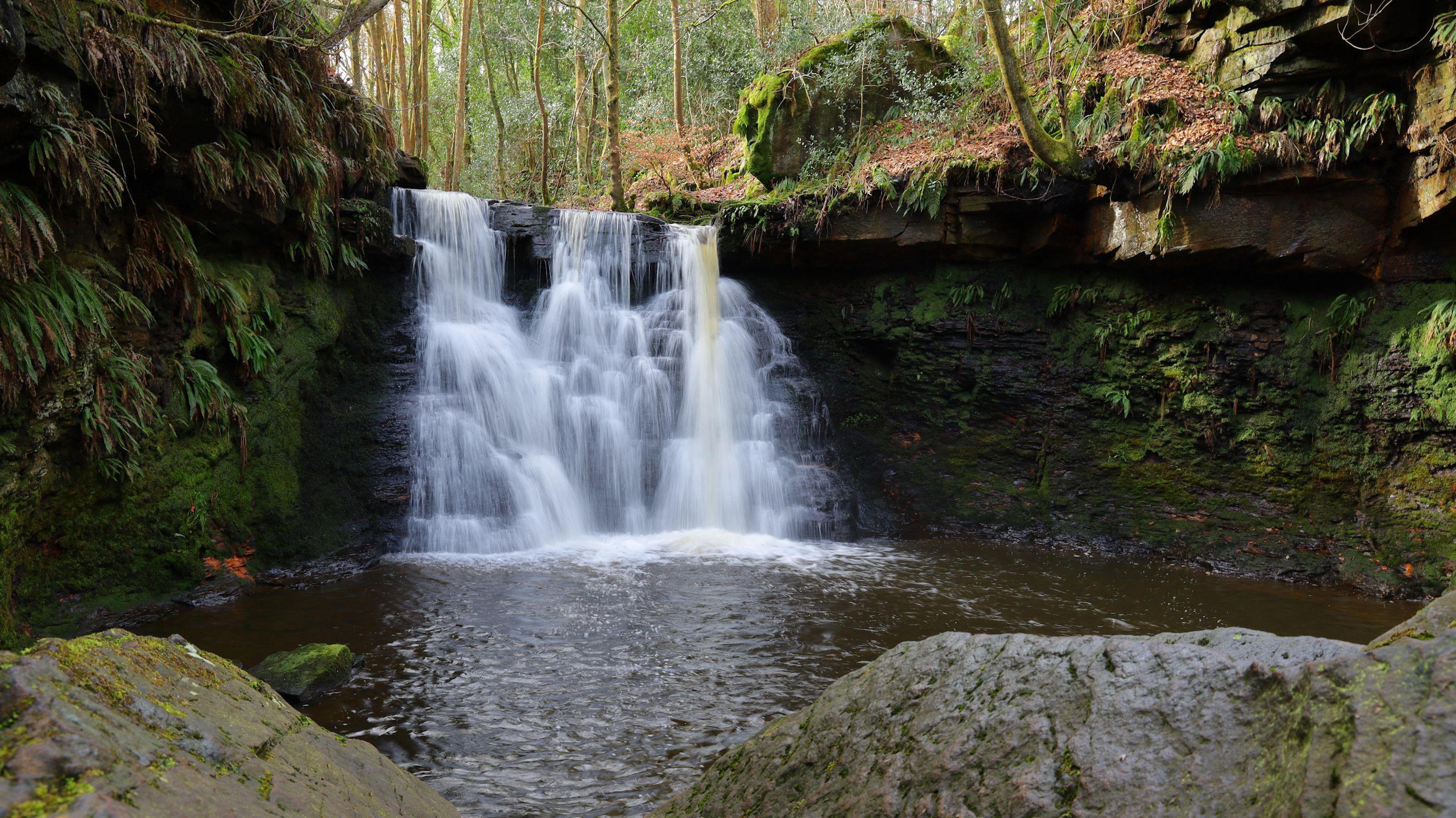 A cascading waterfall and surrounding rocks and woodland