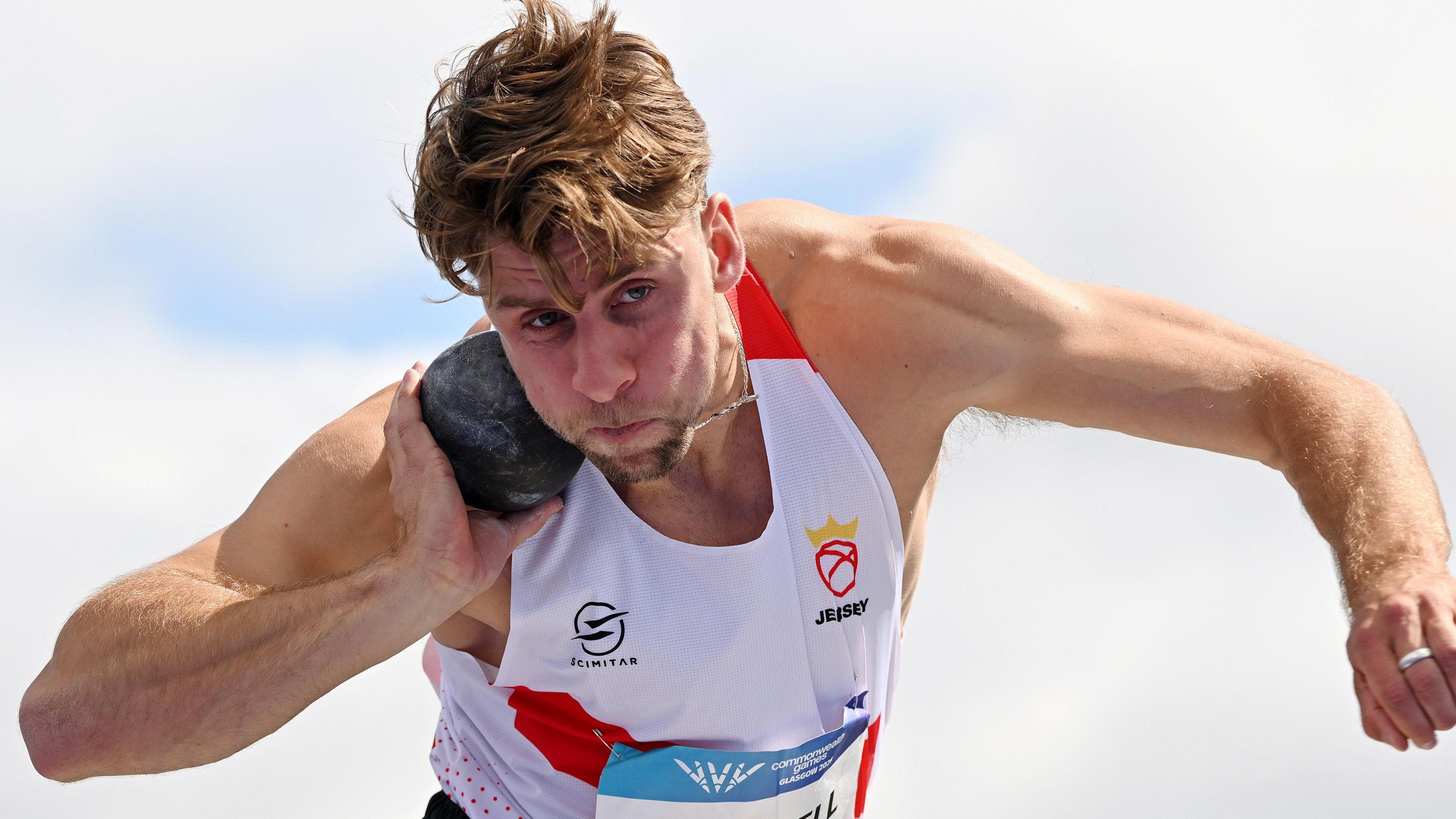 Evan Campbell competes in the shot put wearing a white and red vest