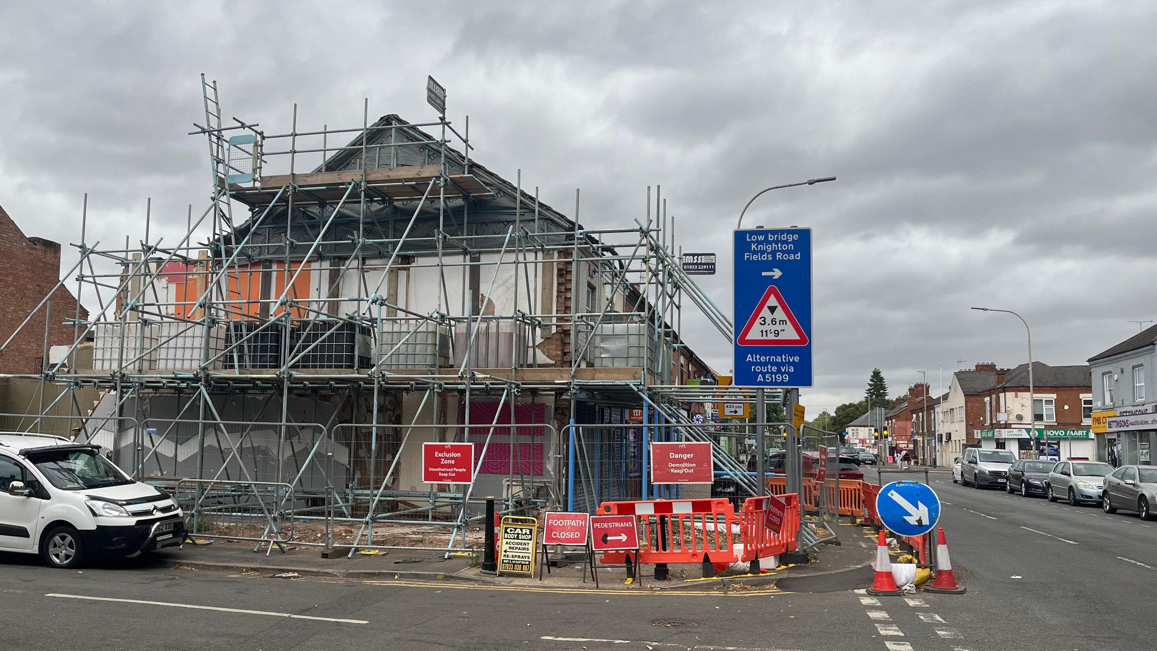 A terraced building with scaffolding on the end and metal wire fences around the site. There are signs diverting pedestrians around the site.